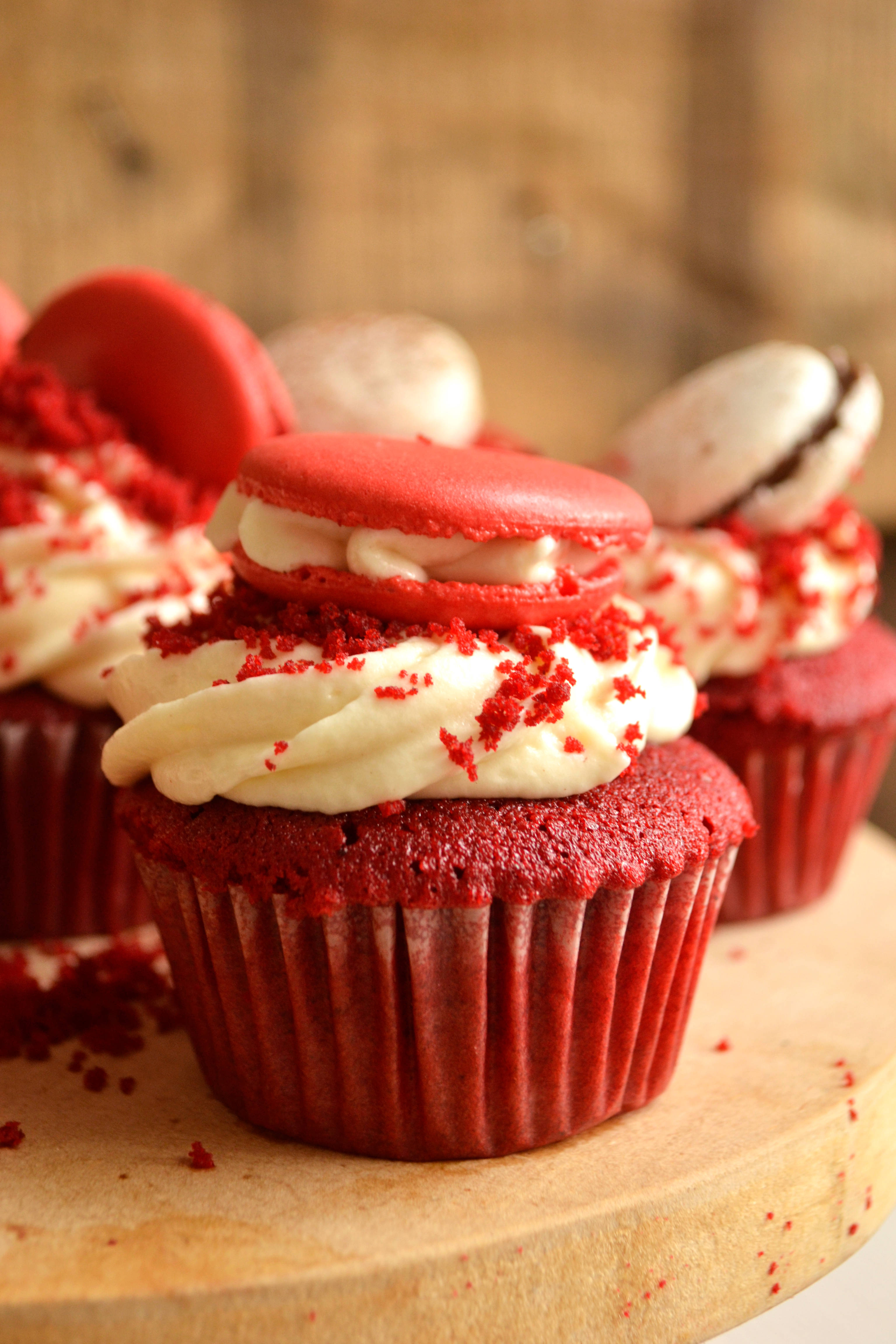 Cupcake 桌布 壁紙 — 豐富的紅絲絨杯子蛋糕，上面有奶油乳酪糖霜和紅色馬卡龍，放在木板上。