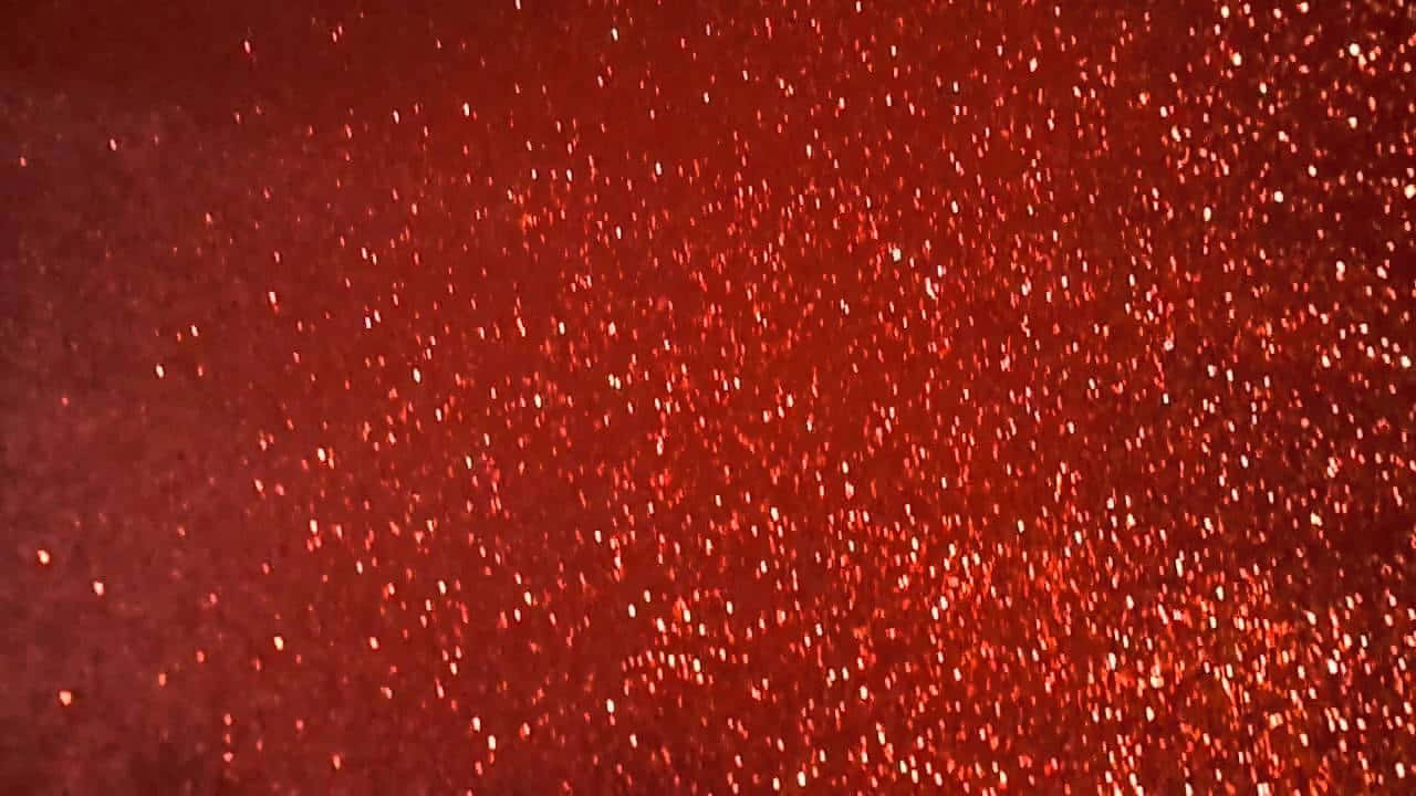 Red Glitter 桌布 壁紙 — 豐富的紅色紋理表面，散落著閃爍的亮粉顆粒，捕捉光線。