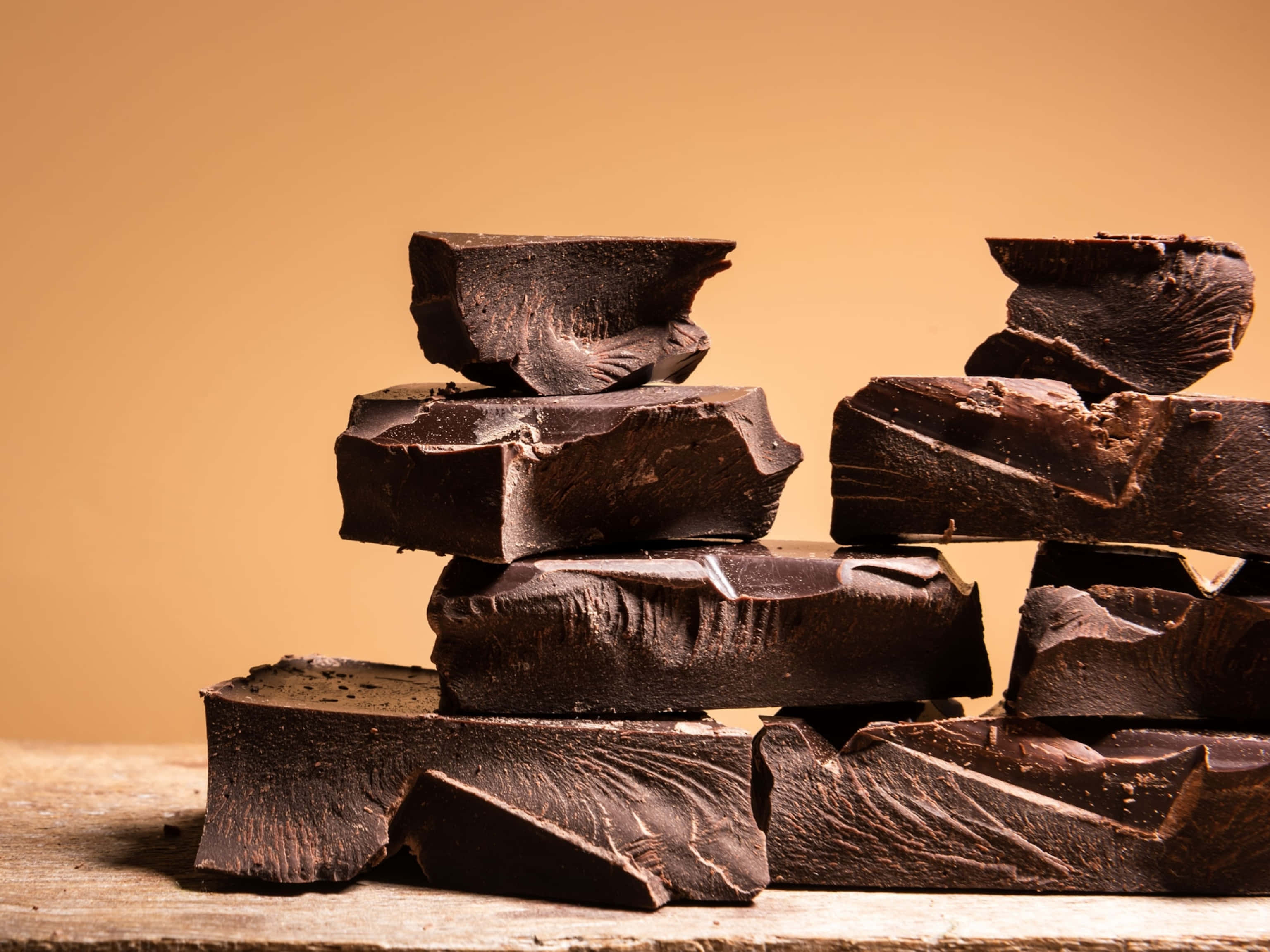 Chocolate 桌布 壁紙 — 豐富的黑巧克力塊堆積在質樸的堆中，放在經風化的木質表面上，背景是溫暖的米色。