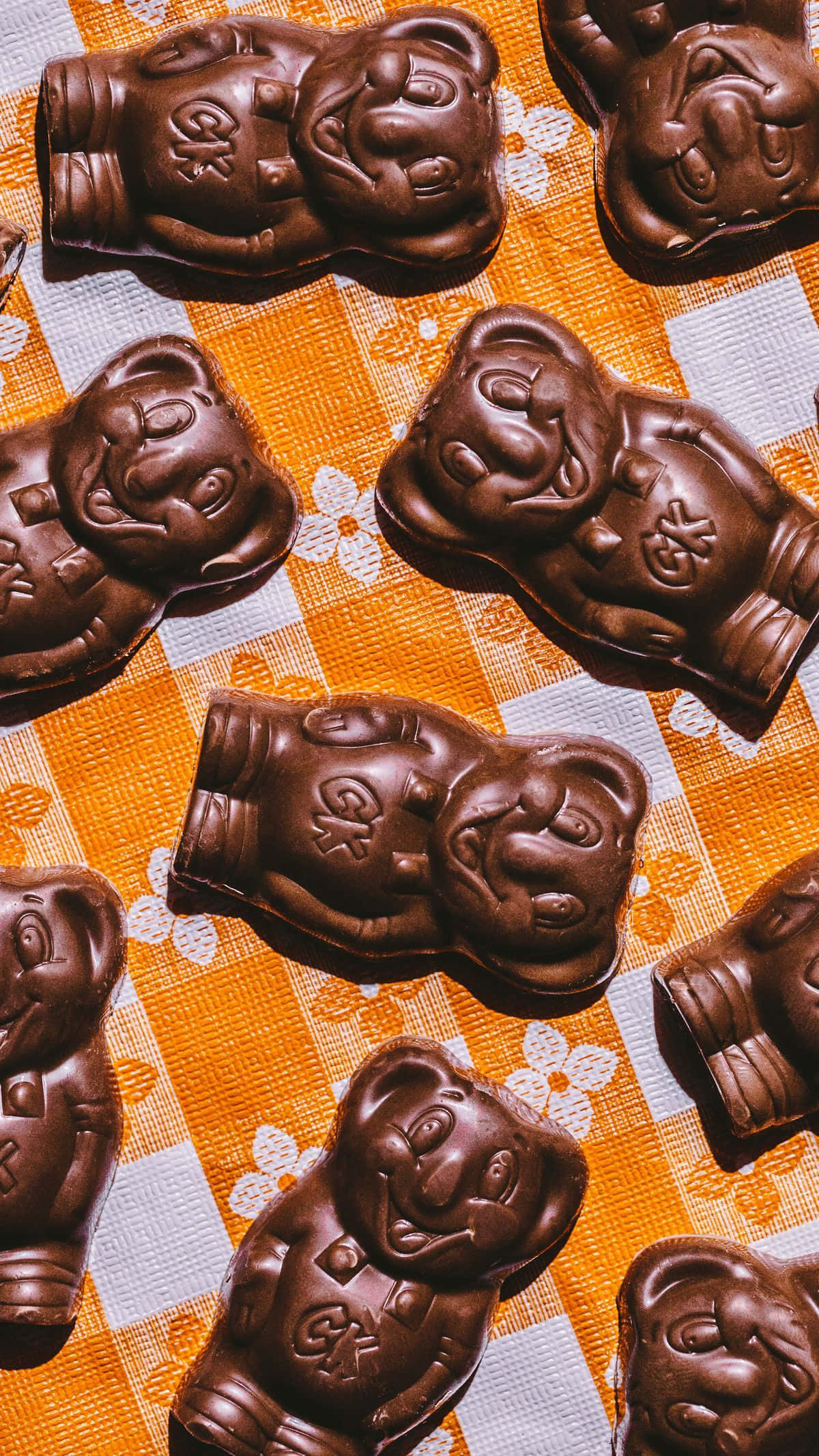 Koala 桌布 壁紙 — 豐富的黑巧克力泰迪熊帶有浮雕臉孔，放在鮮豔的橙色和白色格子桌布上。
