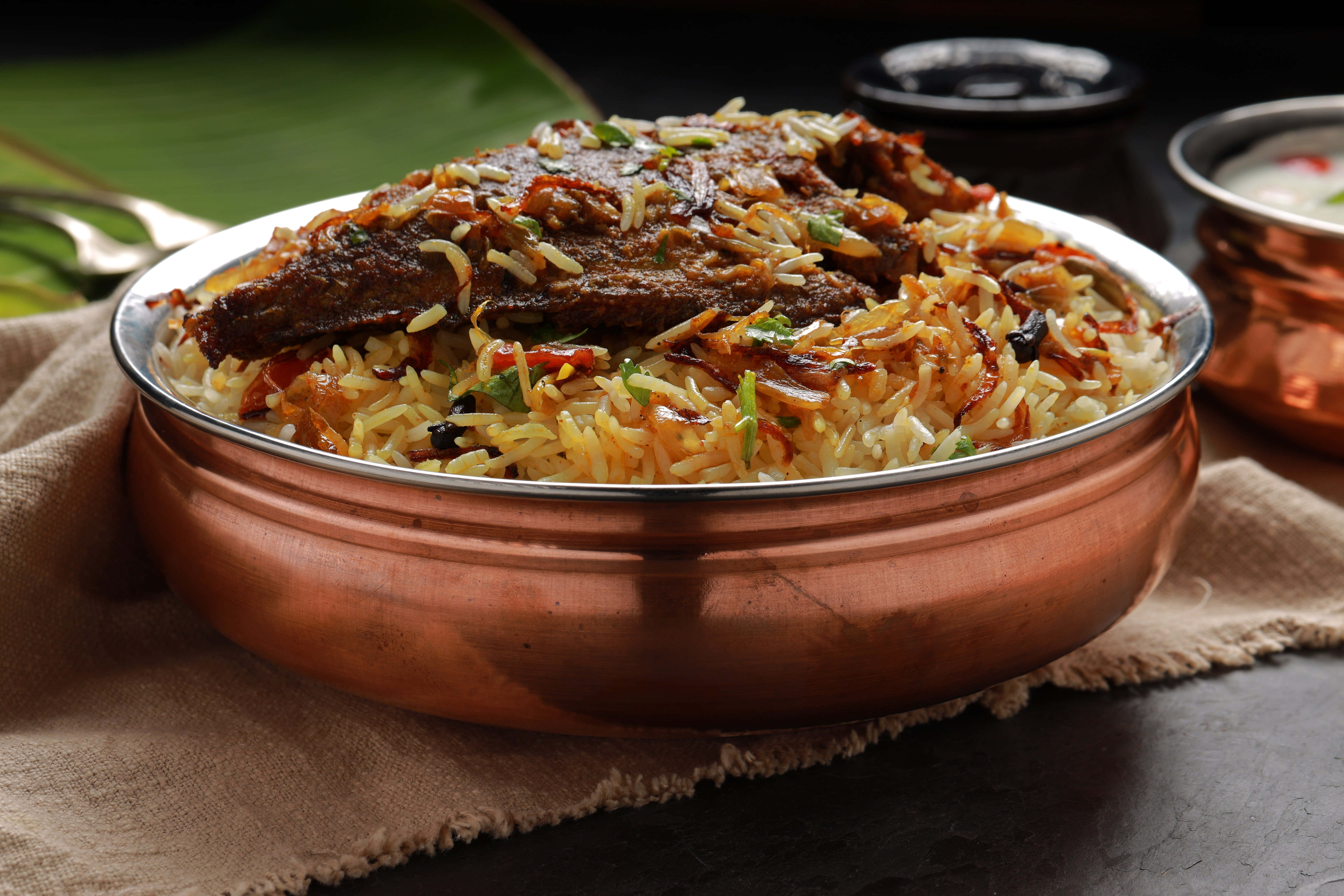 Biryani 桌布 壁紙 — 豐富香料魚肉印度香飯，盛載於閃亮銅碗中，配以裝飾和配菜。