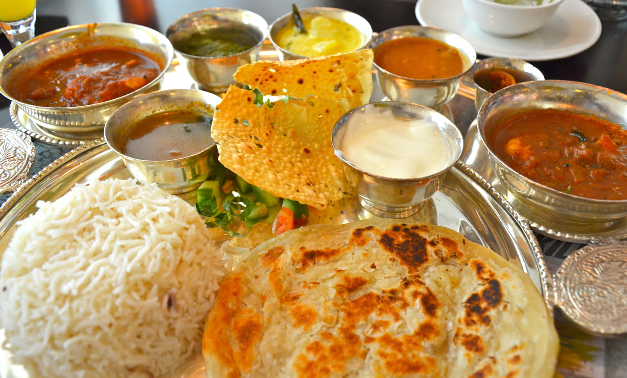 Indian 桌布 壁紙 — 豐盛的印度塔利拼盤，包括米飯、印度烤餅、咖哩和酸辣醬，盛放在閃亮的銀盤上。