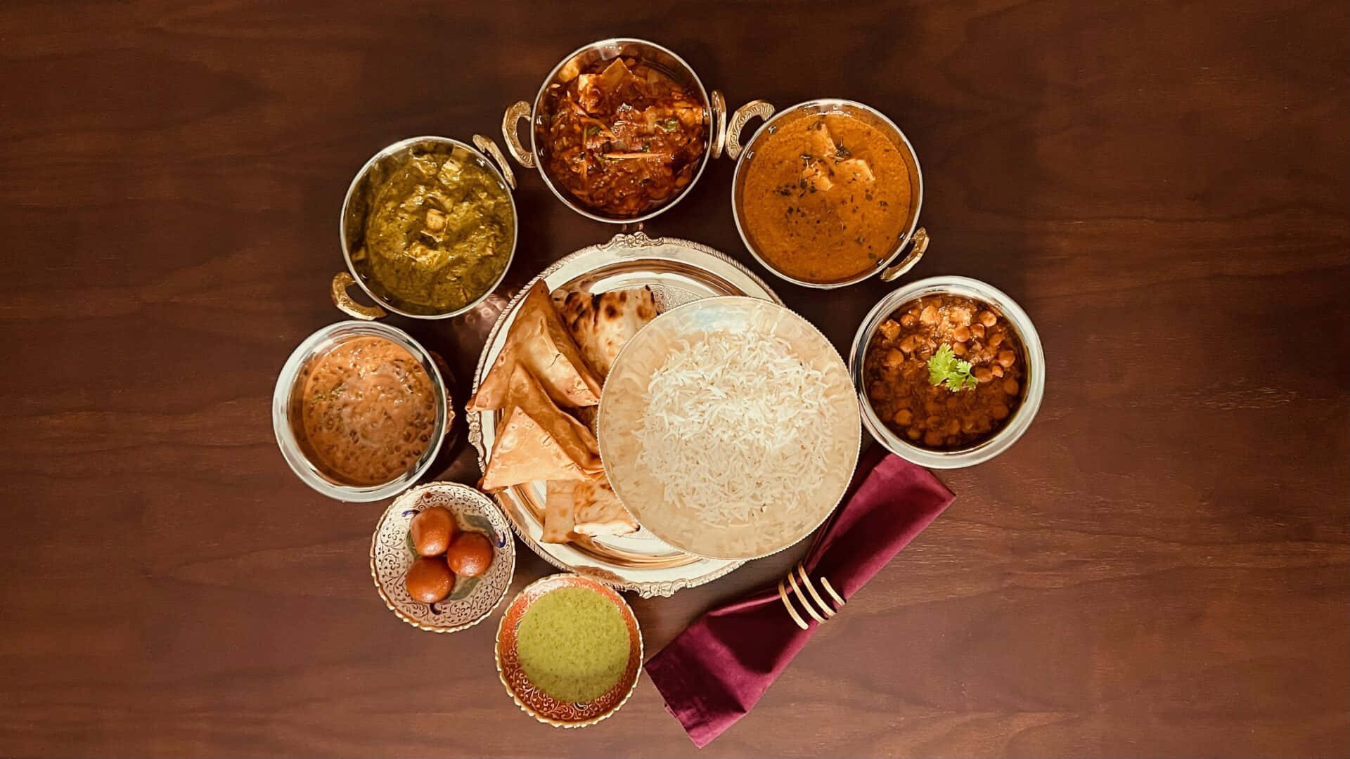 Indian 桌布 壁紙 — 豐盛的印度盛宴，色彩繽紛的咖哩、印度烤餅、米飯和酸辣醬擺放在深色木桌上。