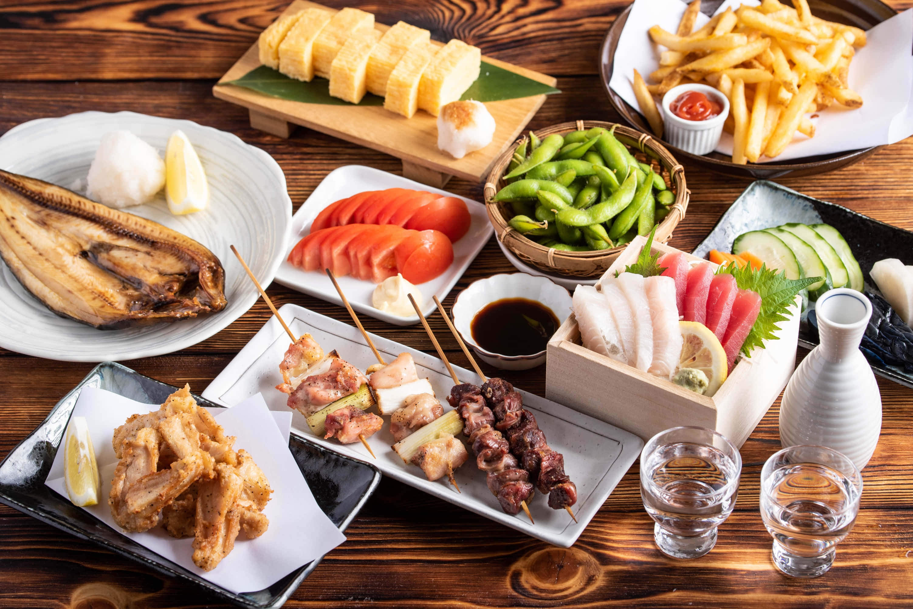 食物動圖 桌布 壁紙 — 豐盛的日本料理，包括烤魚、天婦羅、串燒、毛豆和壽司，擺放在質樸的木桌上。