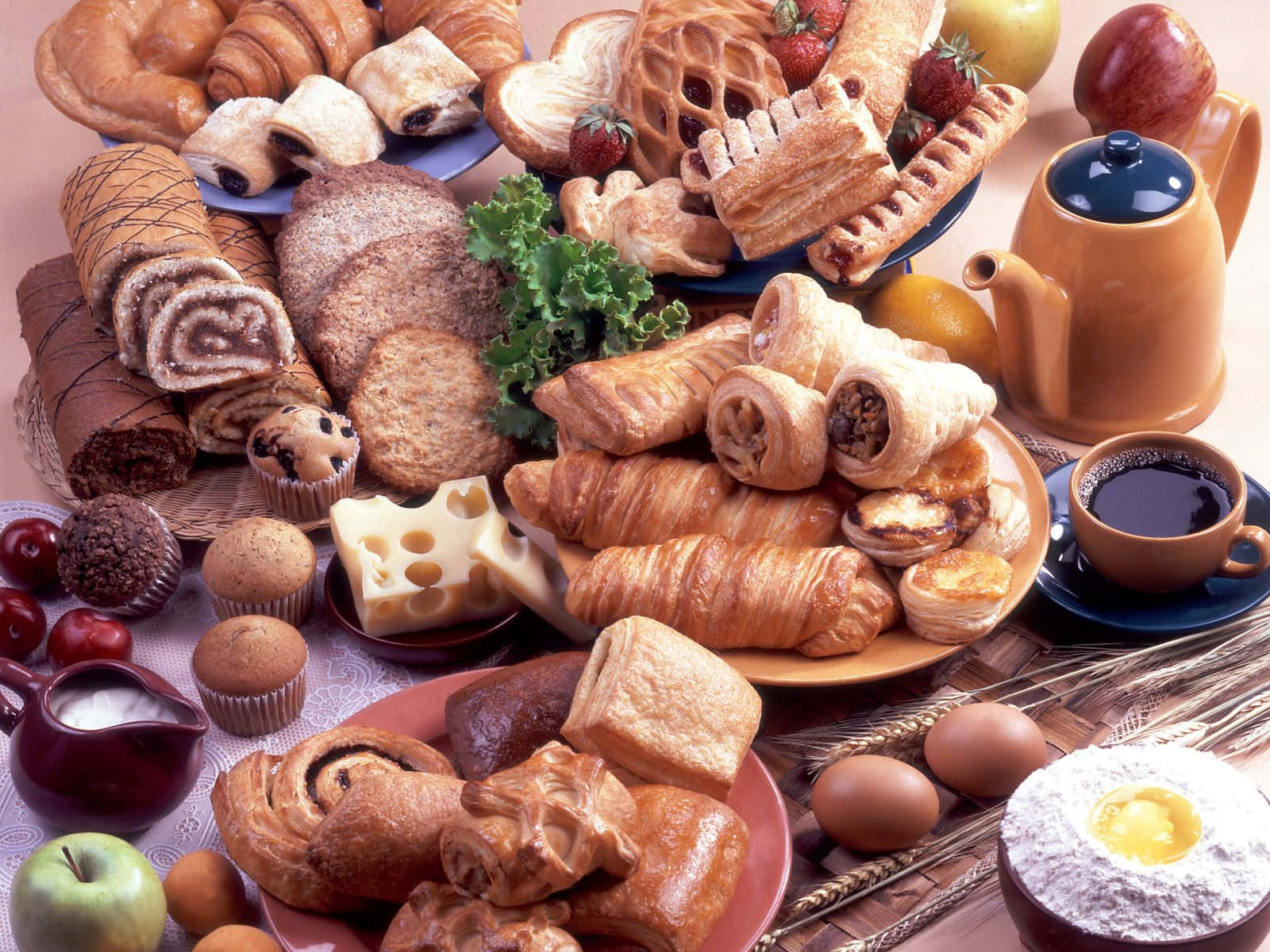Pastries 桌布 壁紙 — 豐盛的早餐擺盤，包括金黃色的可頌、糕點、新鮮水果、起司、雞蛋和咖啡，誘人地擺放在木桌上。