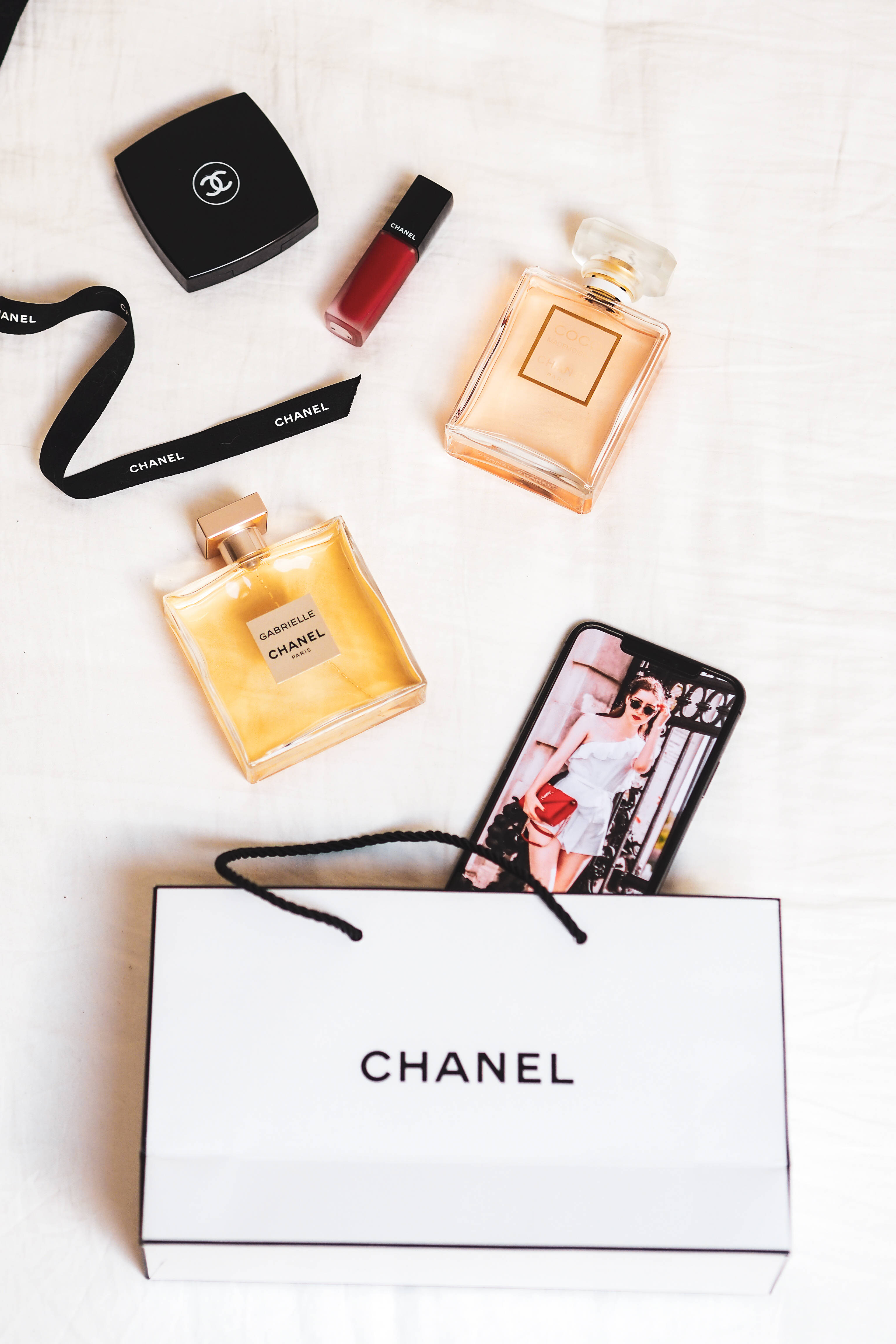 Chanel 桌布 壁紙 — 豪華Chanel美容產品和購物袋整齊地排列在白色紋理表面上。