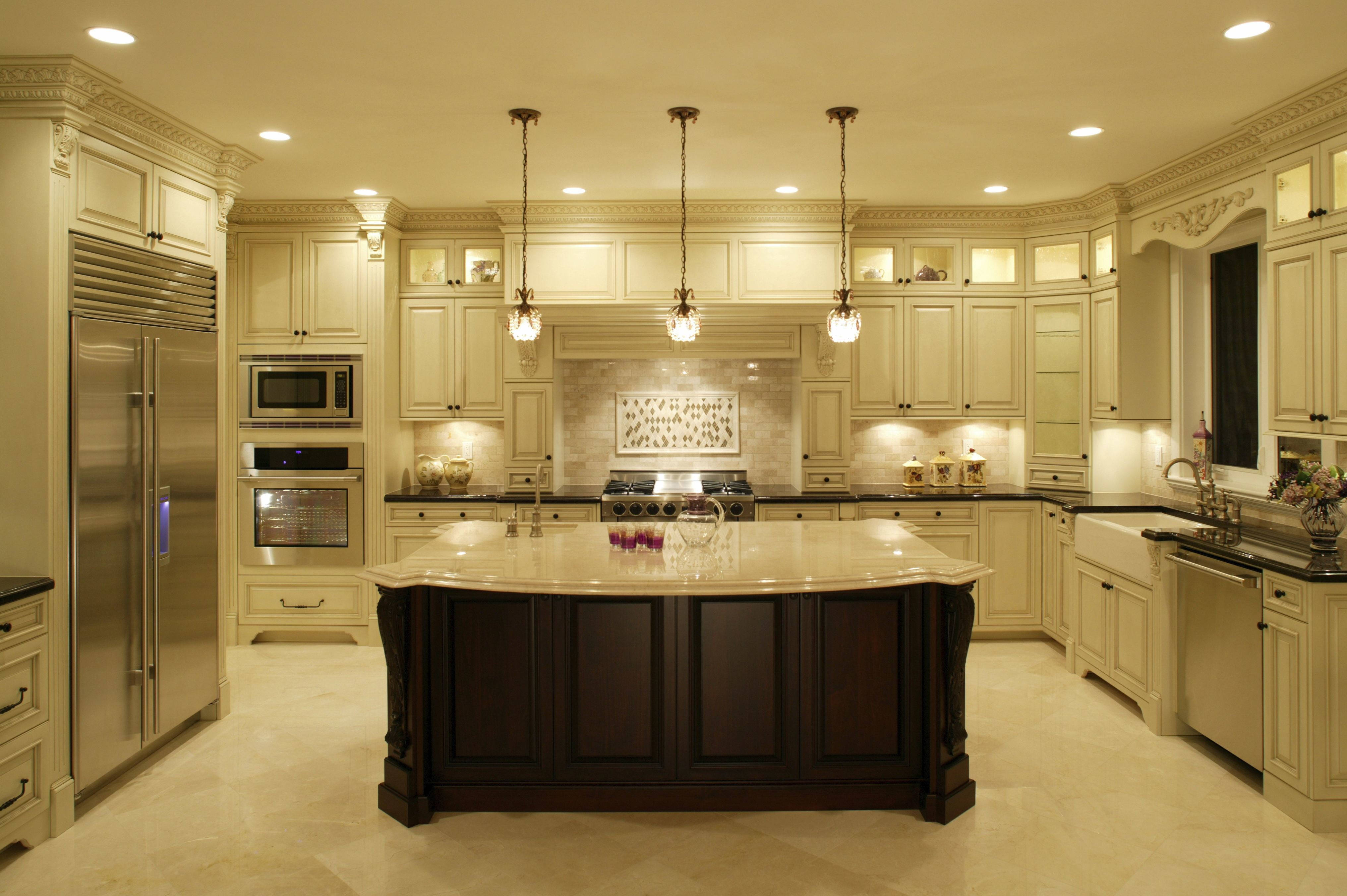 Kitchen Design 桌布 壁紙 — 豪華廚房，配有奶油色櫥櫃、深色木質中島、不鏽鋼電器和溫暖的吊燈照明。