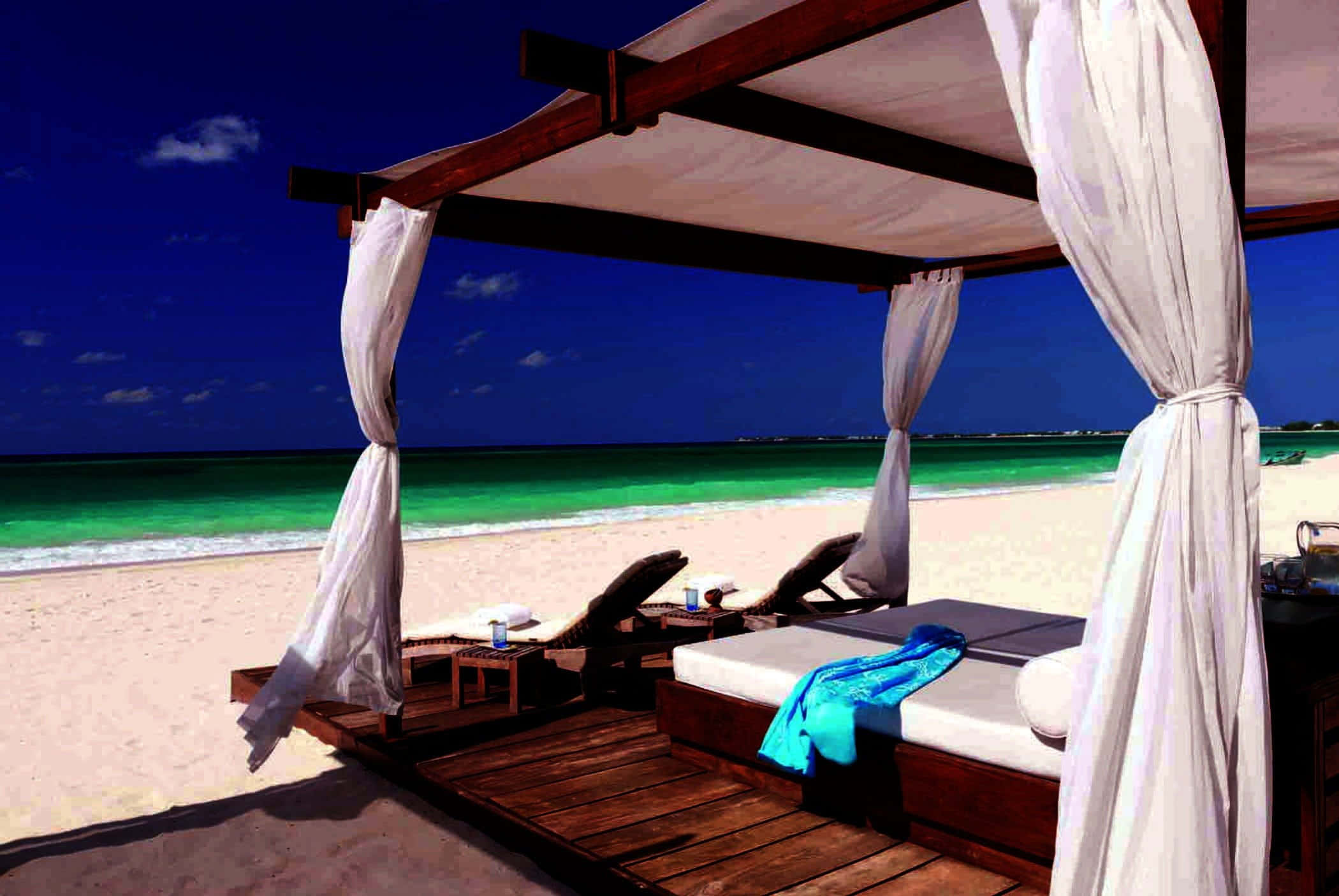 Beach Daybed 桌布 壁紙 — 豪華木製涼亭搭配白色窗簾，俯瞰碧綠的海浪，在湛藍的天空下，純淨的白色沙灘上。