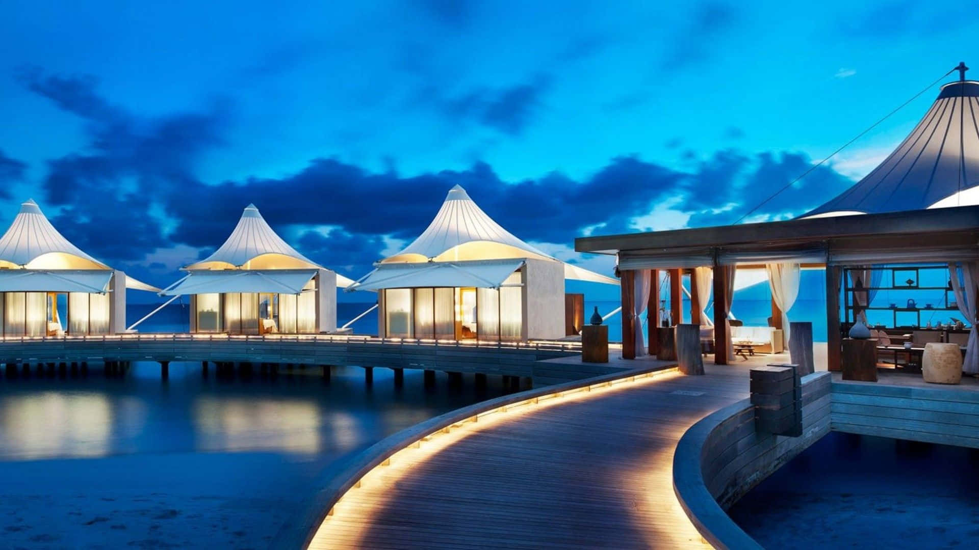 Maldives Beach 桌布 壁紙 — 豪華水上平房在深藍色暮色天空和戲劇性雲彩下溫暖地發光。