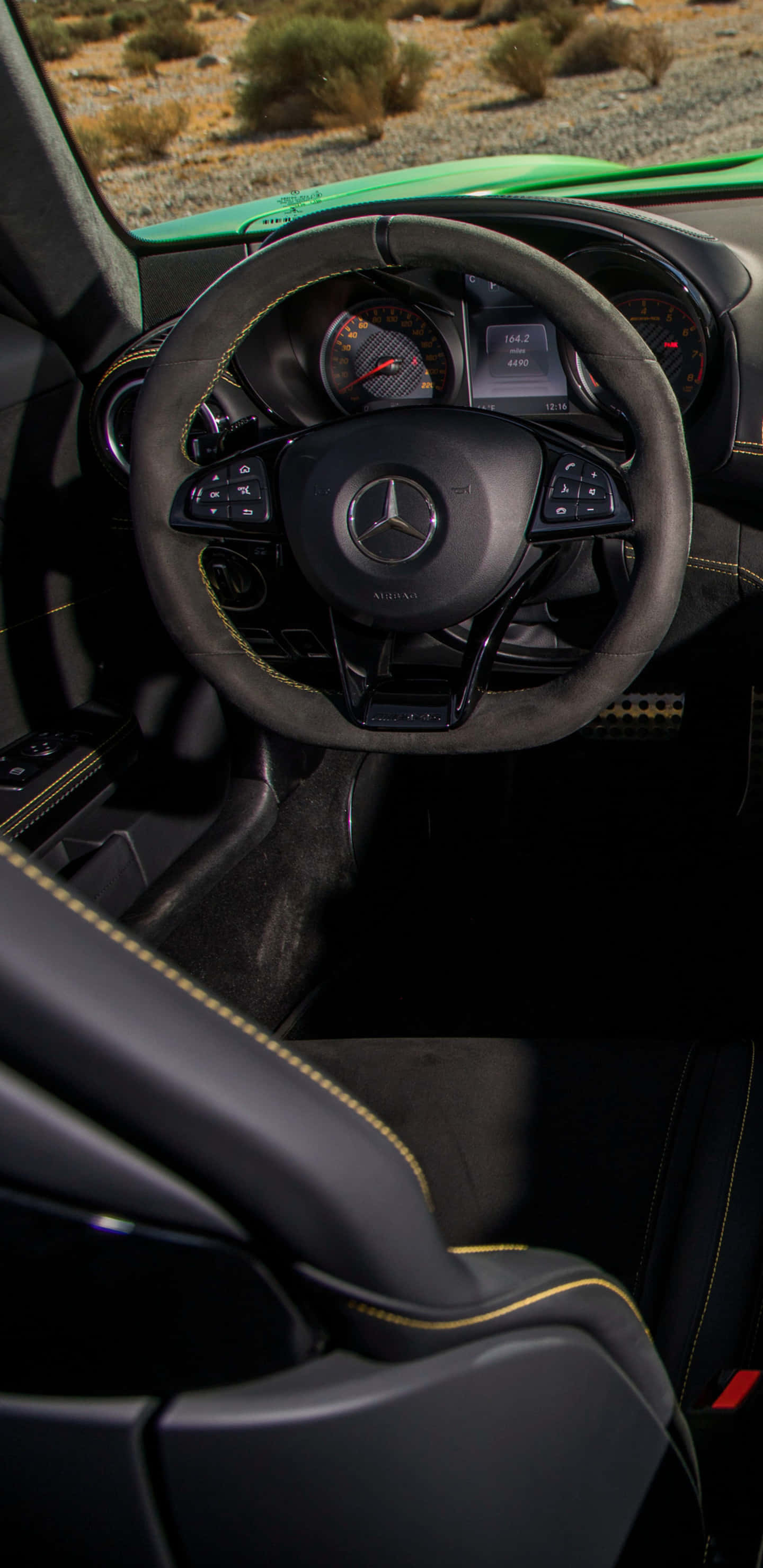 Steering Wheel 桌布 壁紙 — 豪華汽車內部特寫，黑色皮革座椅搭配黃色縫線，從駕駛座視角望向沙漠背景。