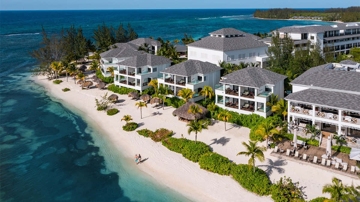 Jamaican Island 桌布 壁紙 — 豪華海濱度假村的鳥瞰圖，白色建築、灰色屋頂和棕櫚樹沿著碧綠海水排列。