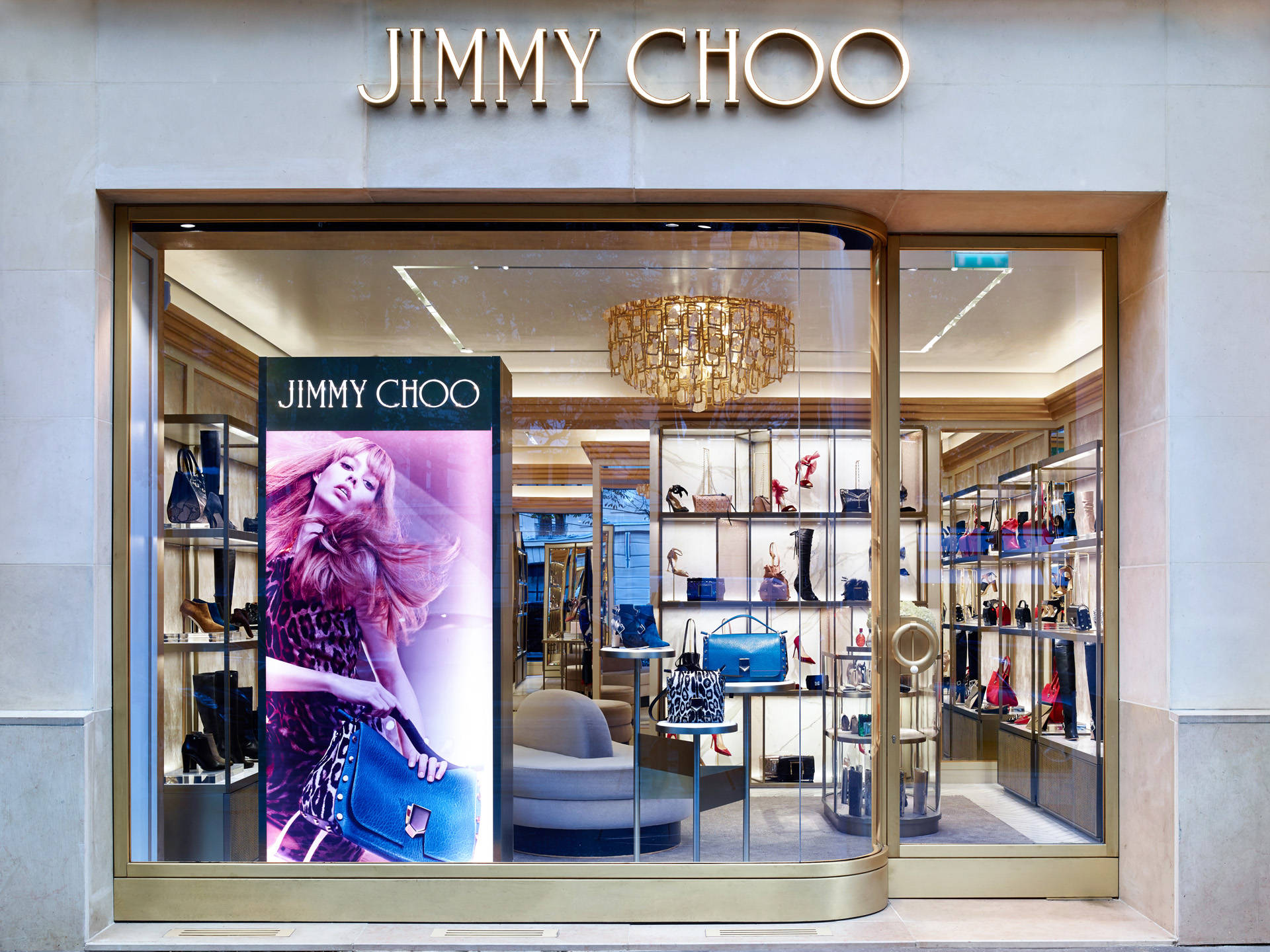 品牌 桌布 壁紙 — 豪華的Jimmy Choo精品店，金色招牌和玻璃櫥窗展示高級手袋和鞋子，在優雅的水晶吊燈照明下。