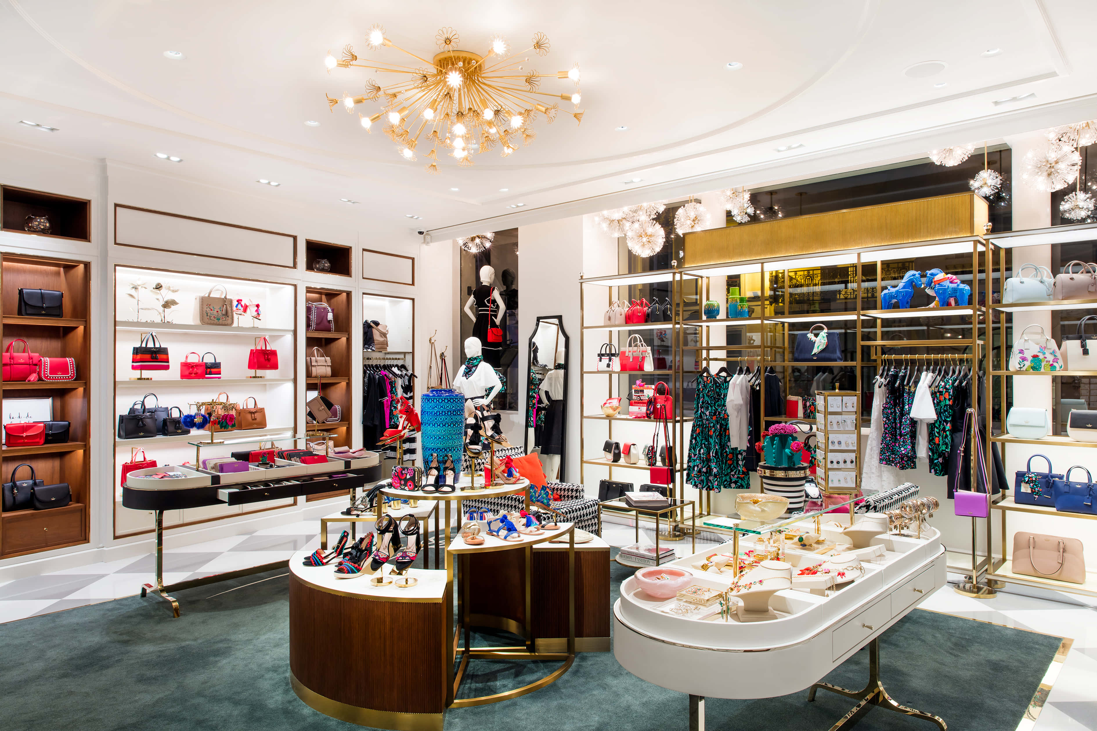kate spade 桌布 壁紙 — 豪華精品店內部，金色裝飾，在優雅吊燈下展示色彩繽紛的手袋、鞋子和服裝。