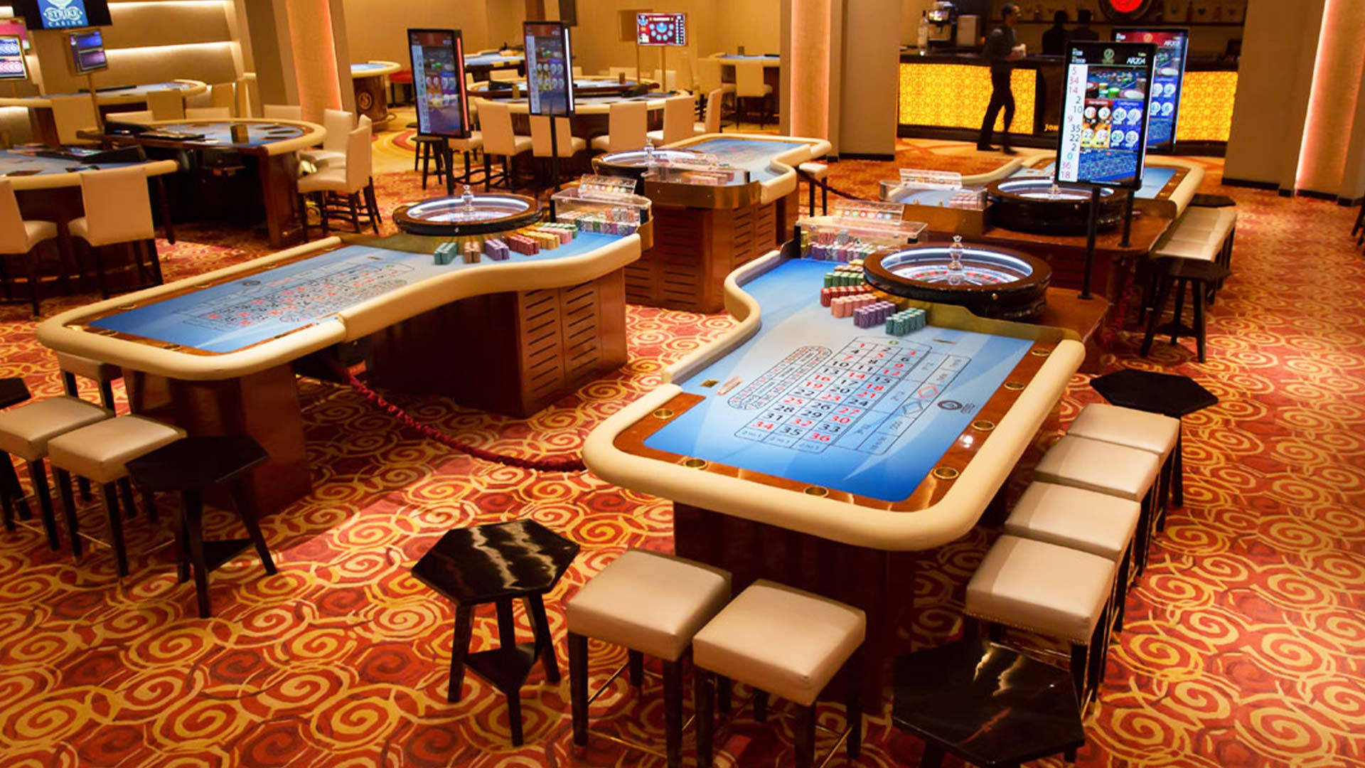 Poker 桌布 壁紙 — 豪華賭場地板，在溫暖的環境燈光下，閃爍的輪盤賭桌和圖案地毯。