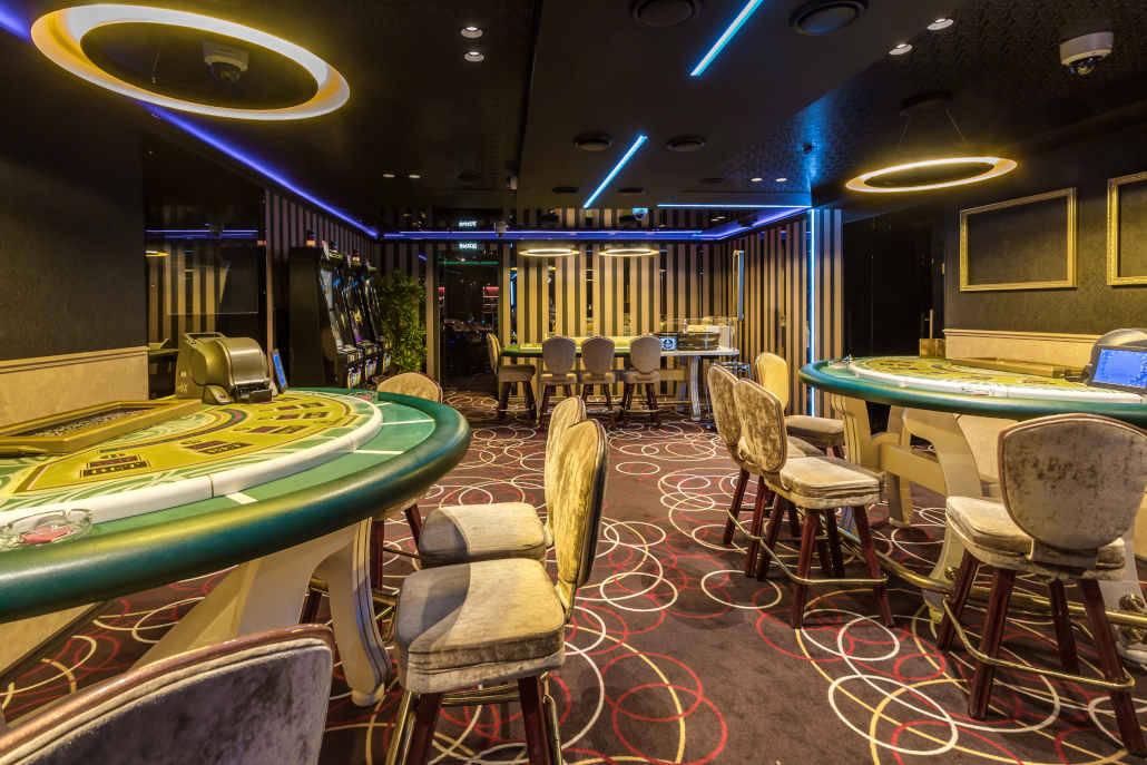 Casino 桌布 壁紙 — 豪華賭場房間，綠色賭桌在圖案地毯上閃爍著霓虹藍和金色燈光。
