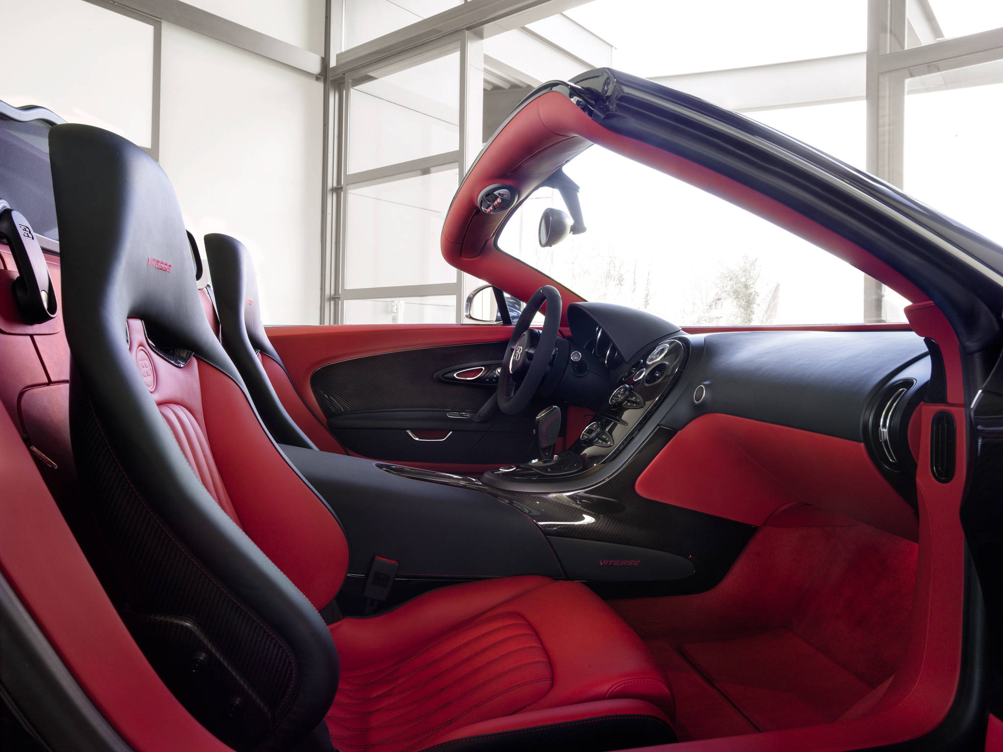 bugatti iPhone 桌布 壁紙 — 豪華跑車內裝，配以鮮明的紅色皮革座椅和黑色碳纖維飾邊，在明亮的日光下。