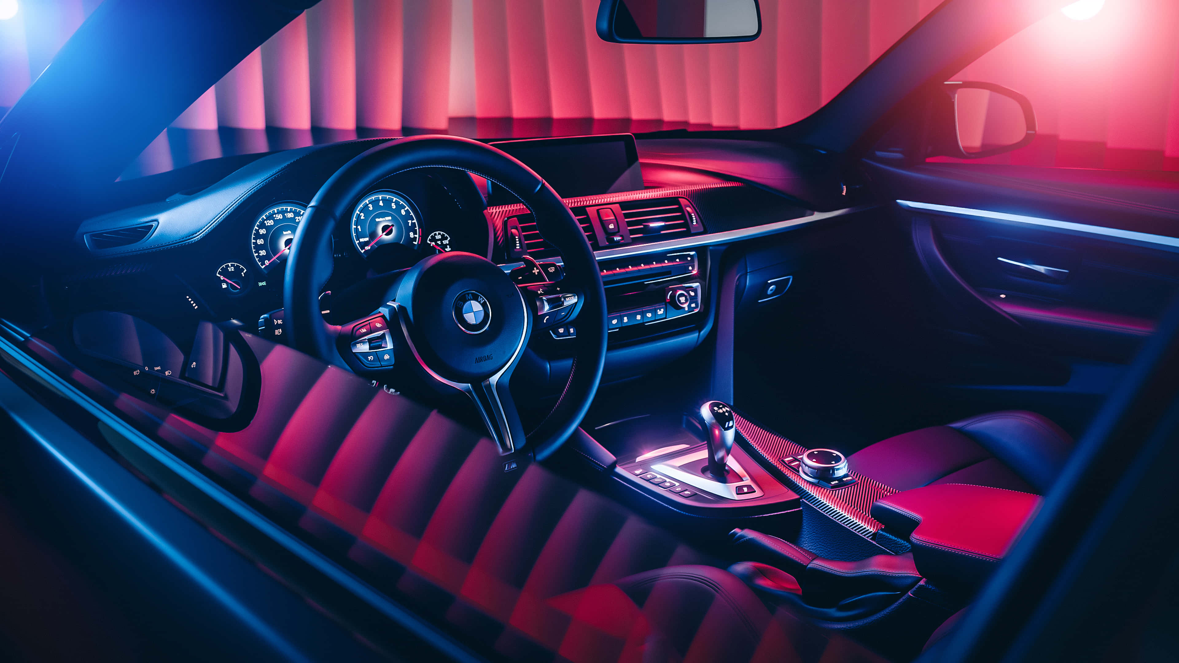 4K BMW 壁紙 桌布 壁紙 — 豪華車內裝沐浴在鮮豔的紅色和藍色霓虹燈光下，突顯時尚的儀表板和運動座椅。