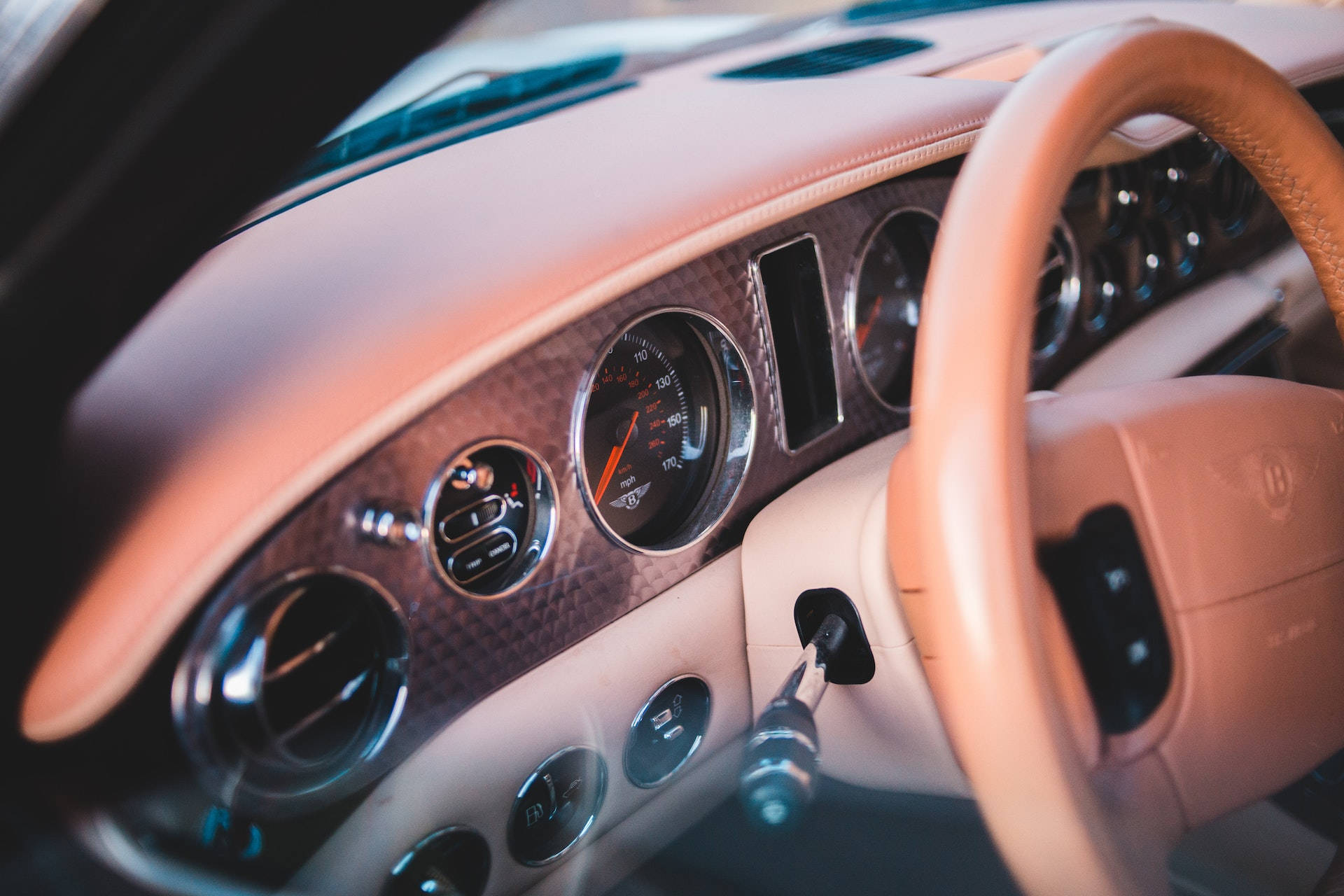 Bentley Cars 桌布 壁紙 — 豪華車內裝特寫，暖色燈光下，棕褐色皮革方向盤和碳纖維儀表板。