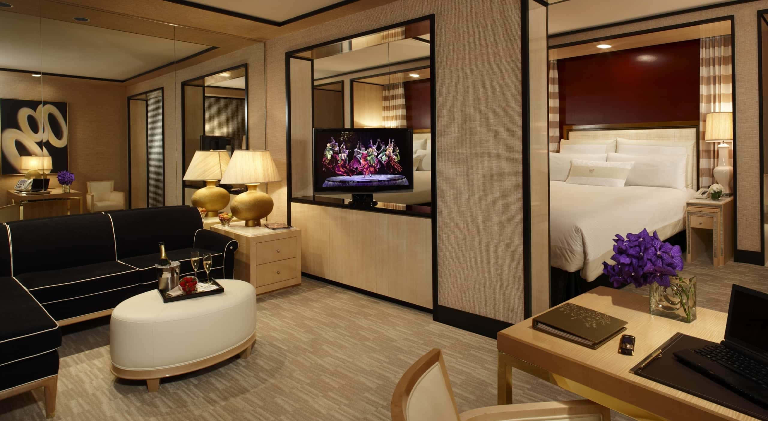 Hotel Room 桌布 壁紙 — 豪華酒店套房，配備現代家具，包括黑色沙發、白色腳凳、電視床和紫色花卉佈置。