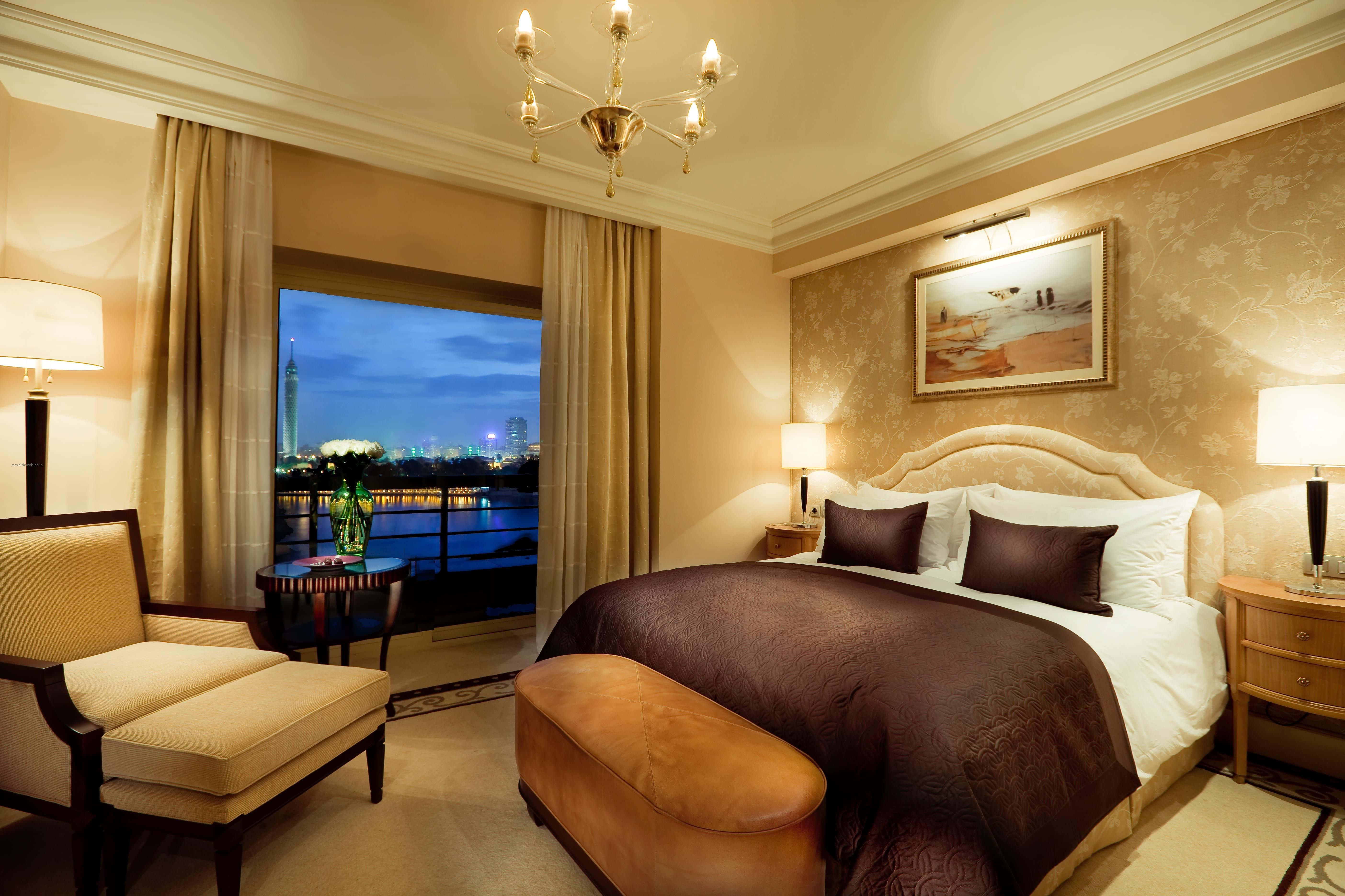 Hotel Room 桌布 壁紙 — 豪華酒店臥室，配備優雅家具，可欣賞黃昏時分的城市景觀。