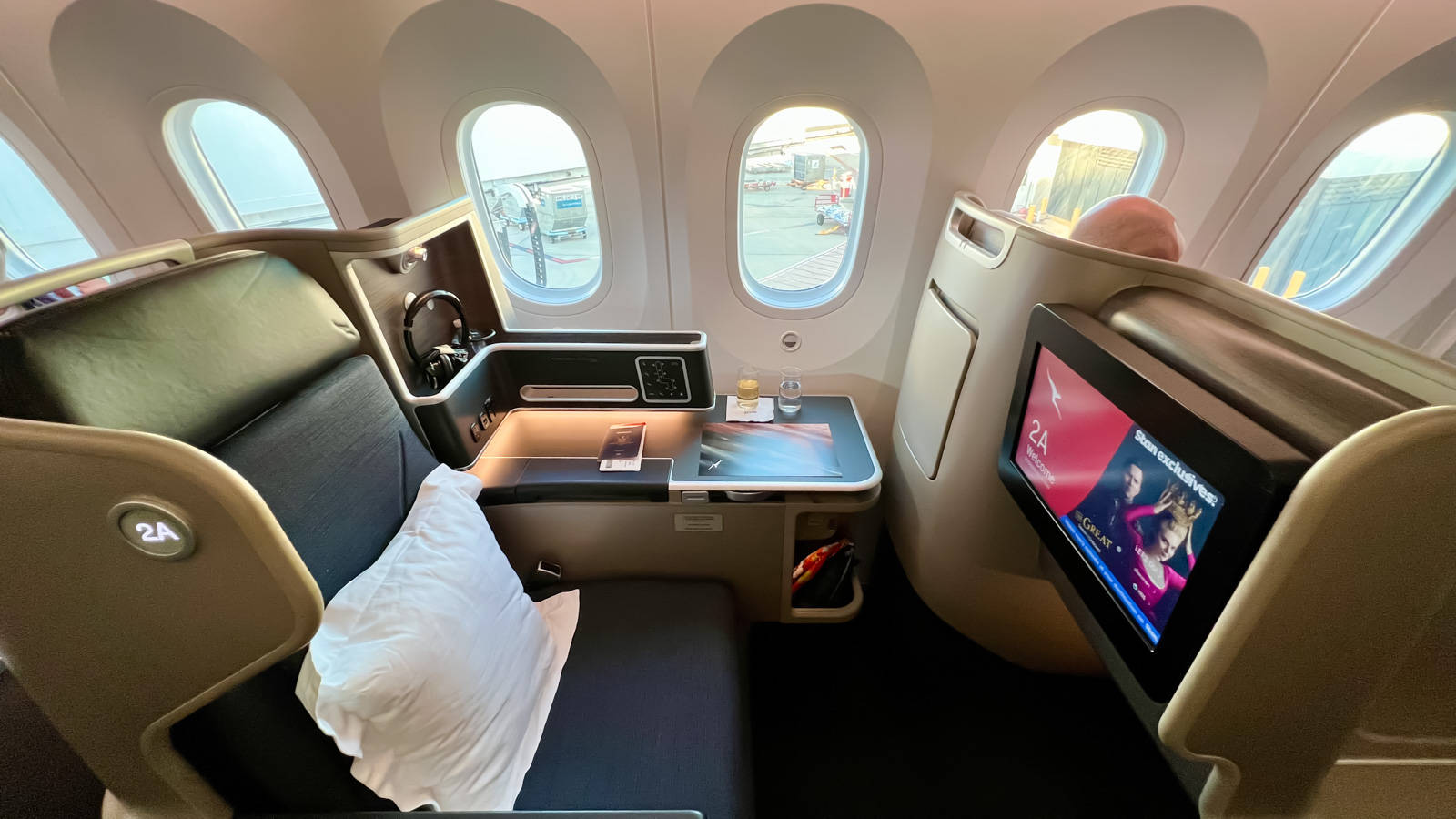 Plane 桌布 壁紙 — 豪華飛機商務艙座位，配有可傾斜的皮革座椅、個人螢幕和可欣賞機場停機坪的窗景。