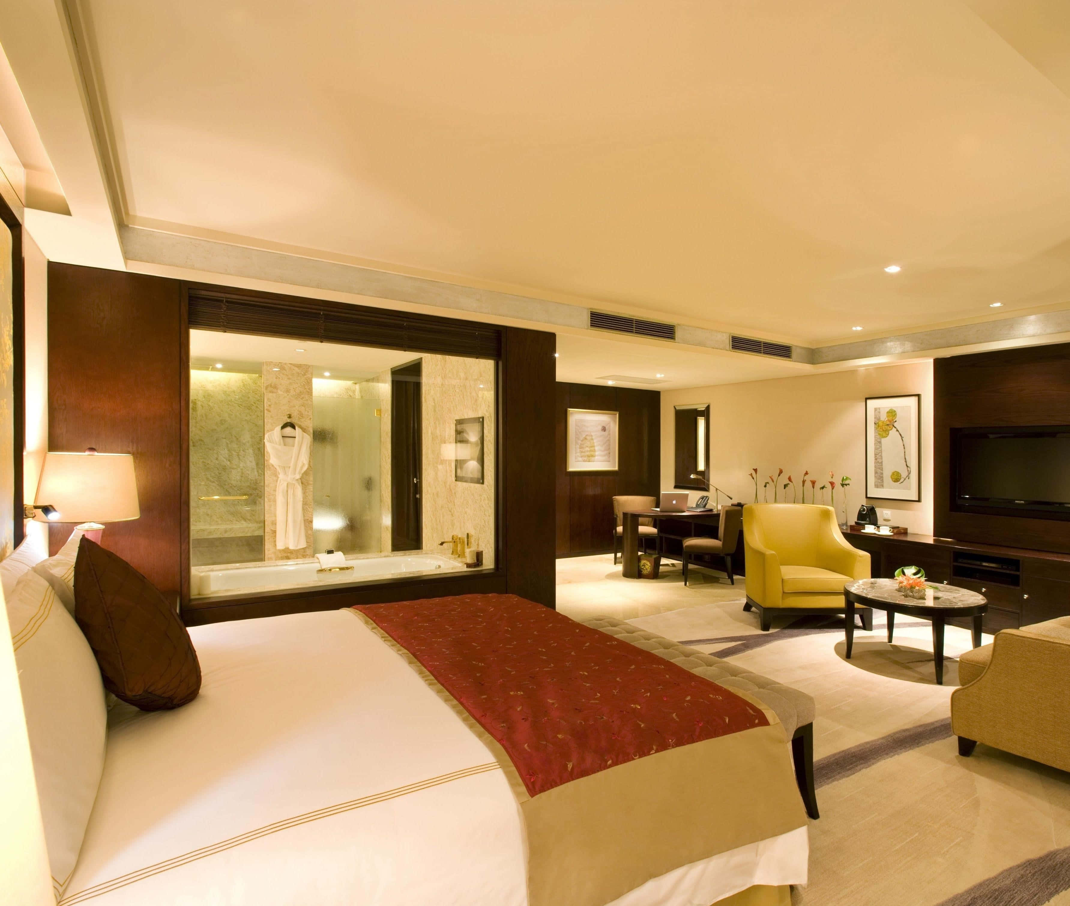 Hotel Room 桌布 壁紙 — 豪華飯店套房，配備大床、玻璃圍封浴室及現代家具，在溫暖環境燈光下。