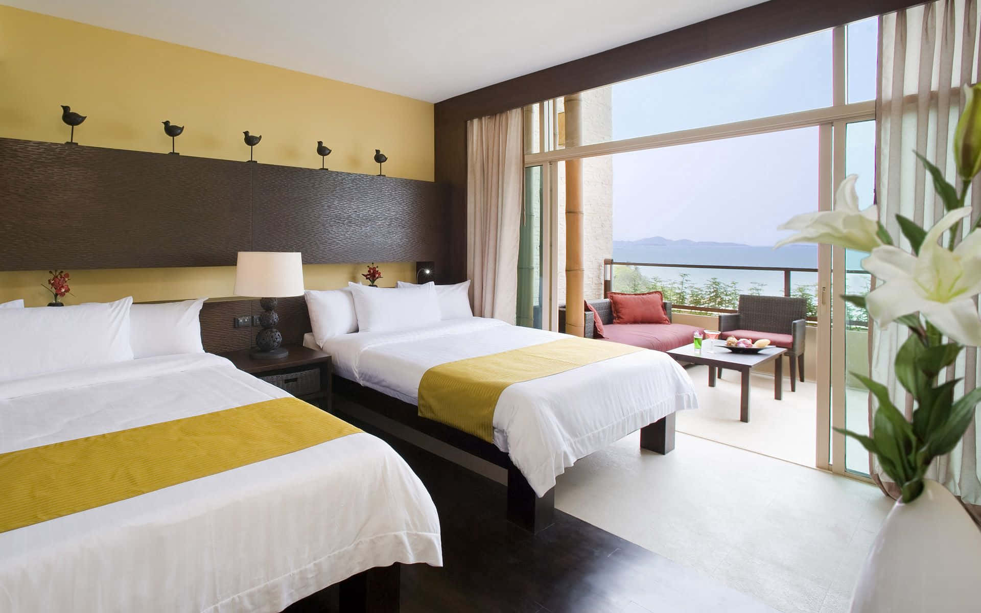 Bedroom 桌布 壁紙 — 豪華飯店客房，設有兩張床、黃色點綴和可俯瞰海洋和山脈的陽台。