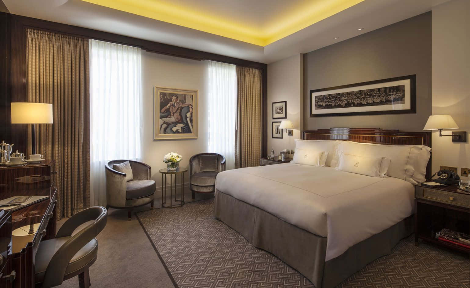Hotel Room 桌布 壁紙 — 豪華飯店客房，配備一張大床、優雅家具，以及來自天花板和床頭燈的溫暖環境照明。