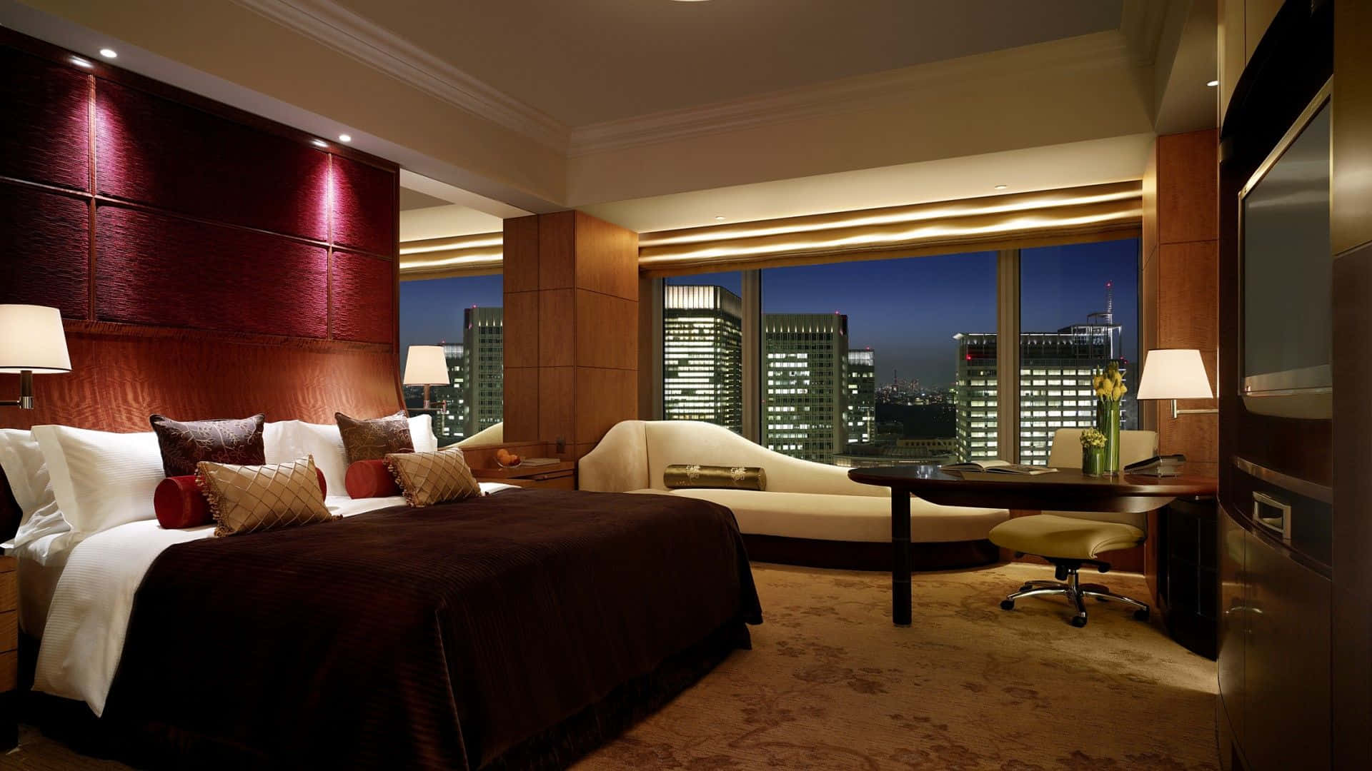 Hotel Room 桌布 壁紙 — 豪華飯店臥室，配有深紅色床頭板和夜晚的城市天際線景觀。