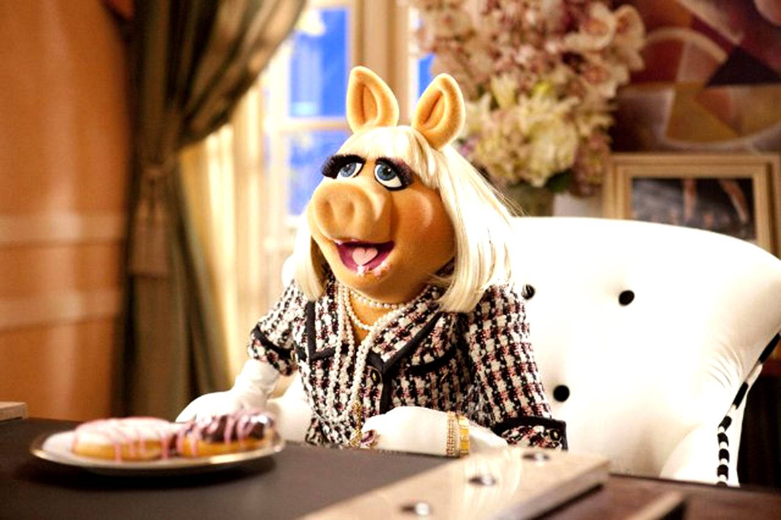 Miss Piggy 桌布 壁紙 — 豬小姐優雅地坐在白色椅子上，穿著時尚的黑白格紋西裝，佩戴珍珠，微笑著看著一盤甜甜圈。