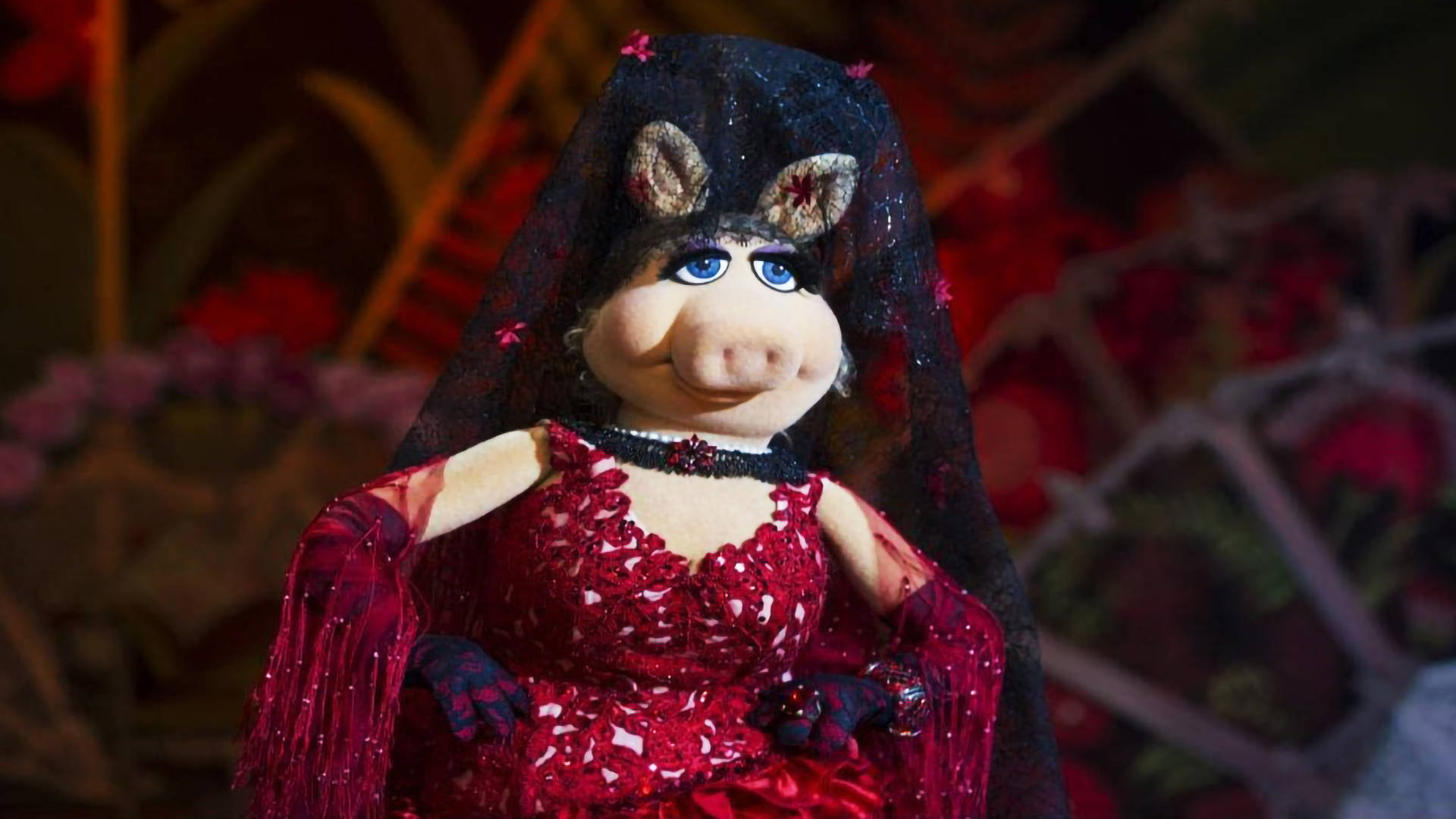 muppets 桌布 壁紙 — 豬小姐身穿閃閃發光的紅色婚紗和帶有花卉裝飾的黑色頭紗，在溫暖的舞台燈光下。
