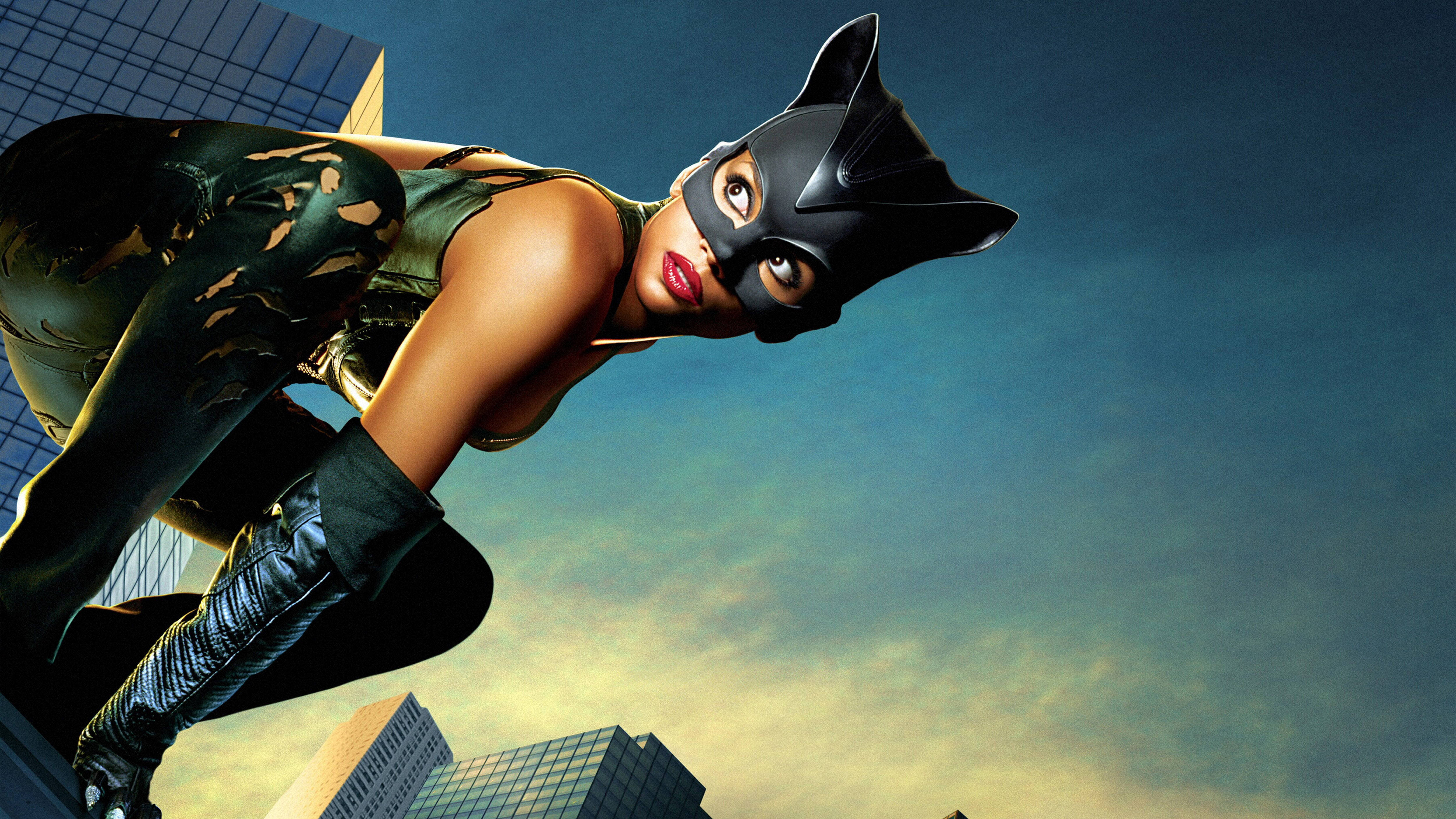 Catwoman 桌布 壁紙 — 貓女坐在摩天大樓頂端，背景是暮色天空，擁有鮮豔的紅唇和時尚的黑色緊身衣。