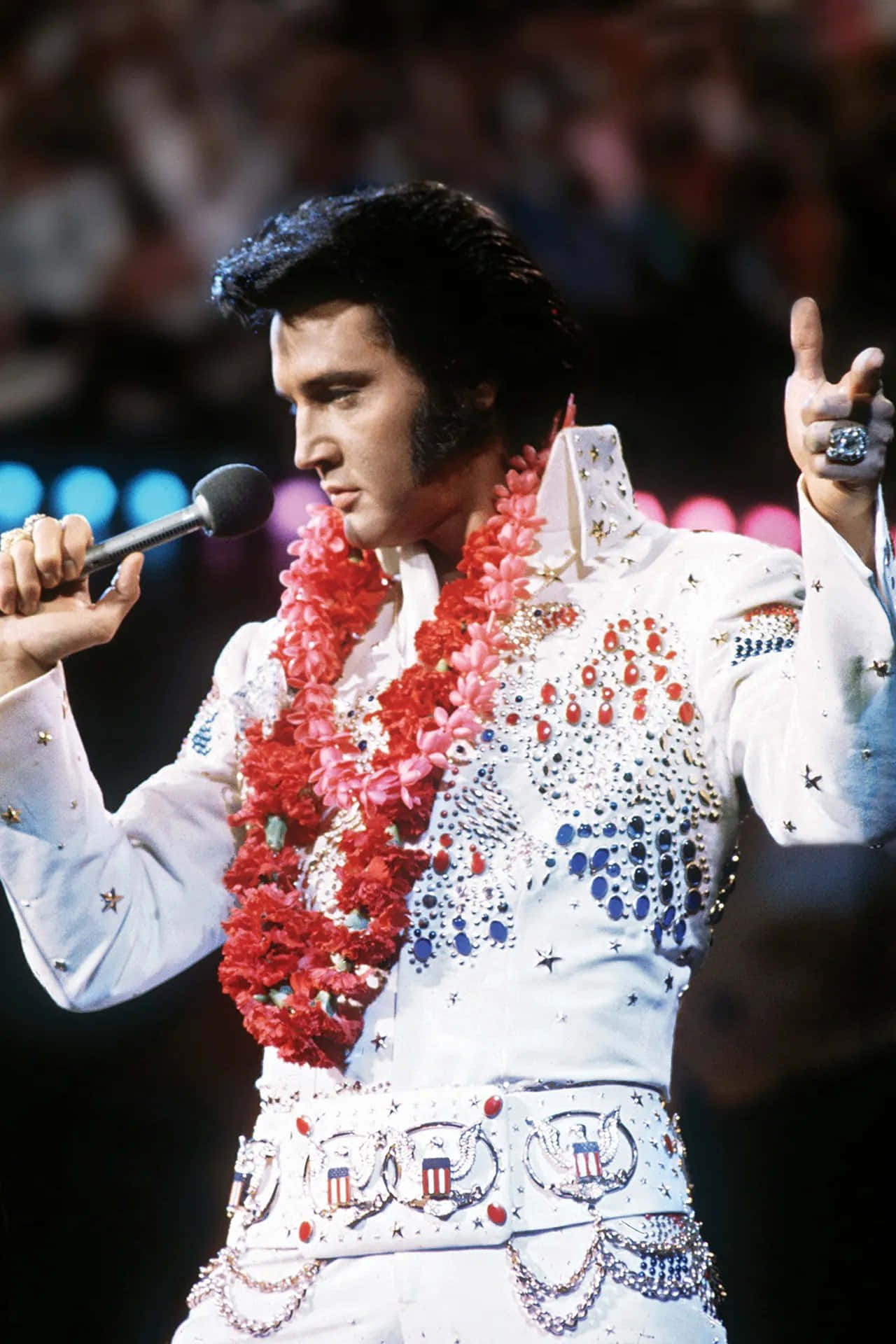 Elvis 桌布 壁紙 — 貓王艾維斯·普里斯萊在明亮的舞台燈光下，身穿飾有紅花和星星的耀眼白色亮片西裝表演。