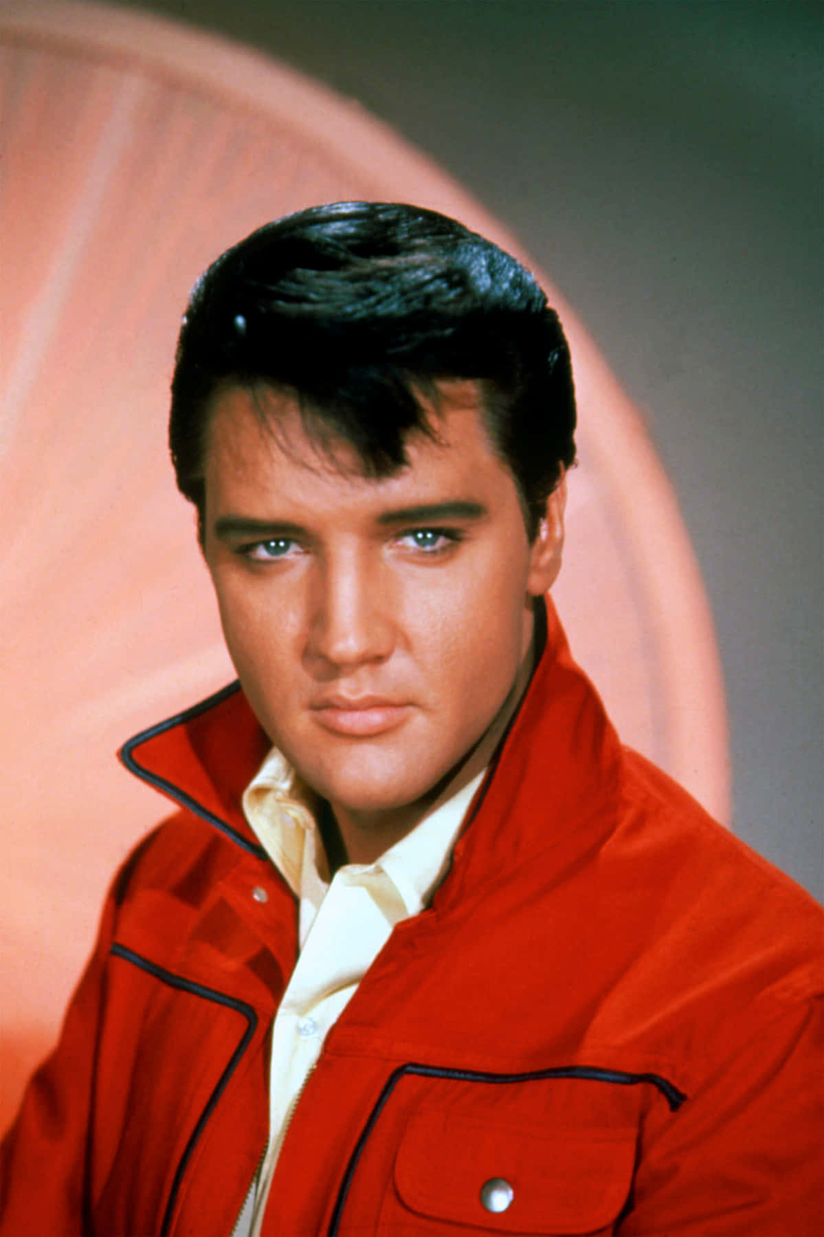 Elvis 桌布 壁紙 — 貓王艾維斯普里斯萊穿著大膽的紅色外套，在柔和的粉紅色弧形背景下凝視著。