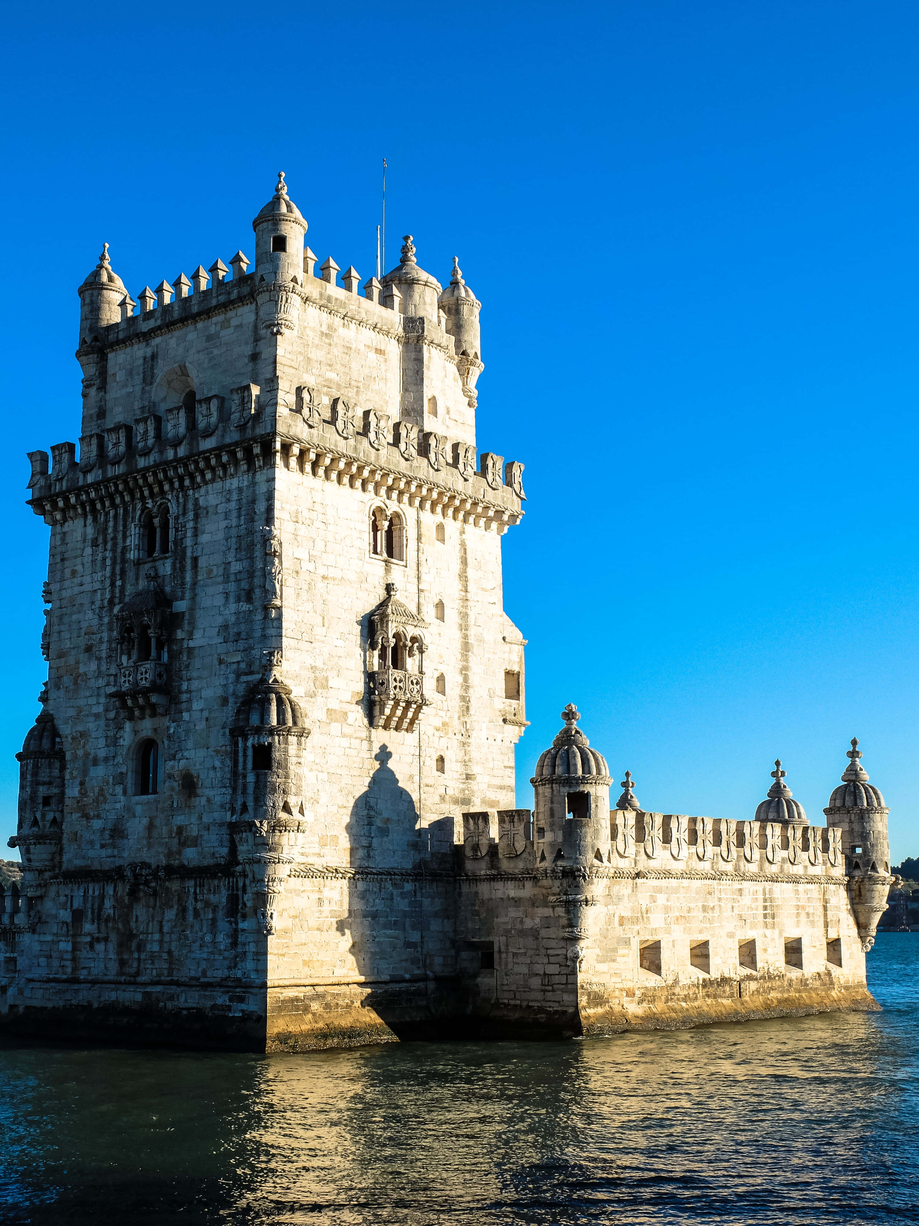 Portugal 桌布 壁紙 — 貝倫塔在晴朗的藍天下雄偉地矗立在特茹河中，陽光突顯其精緻的石造建築。