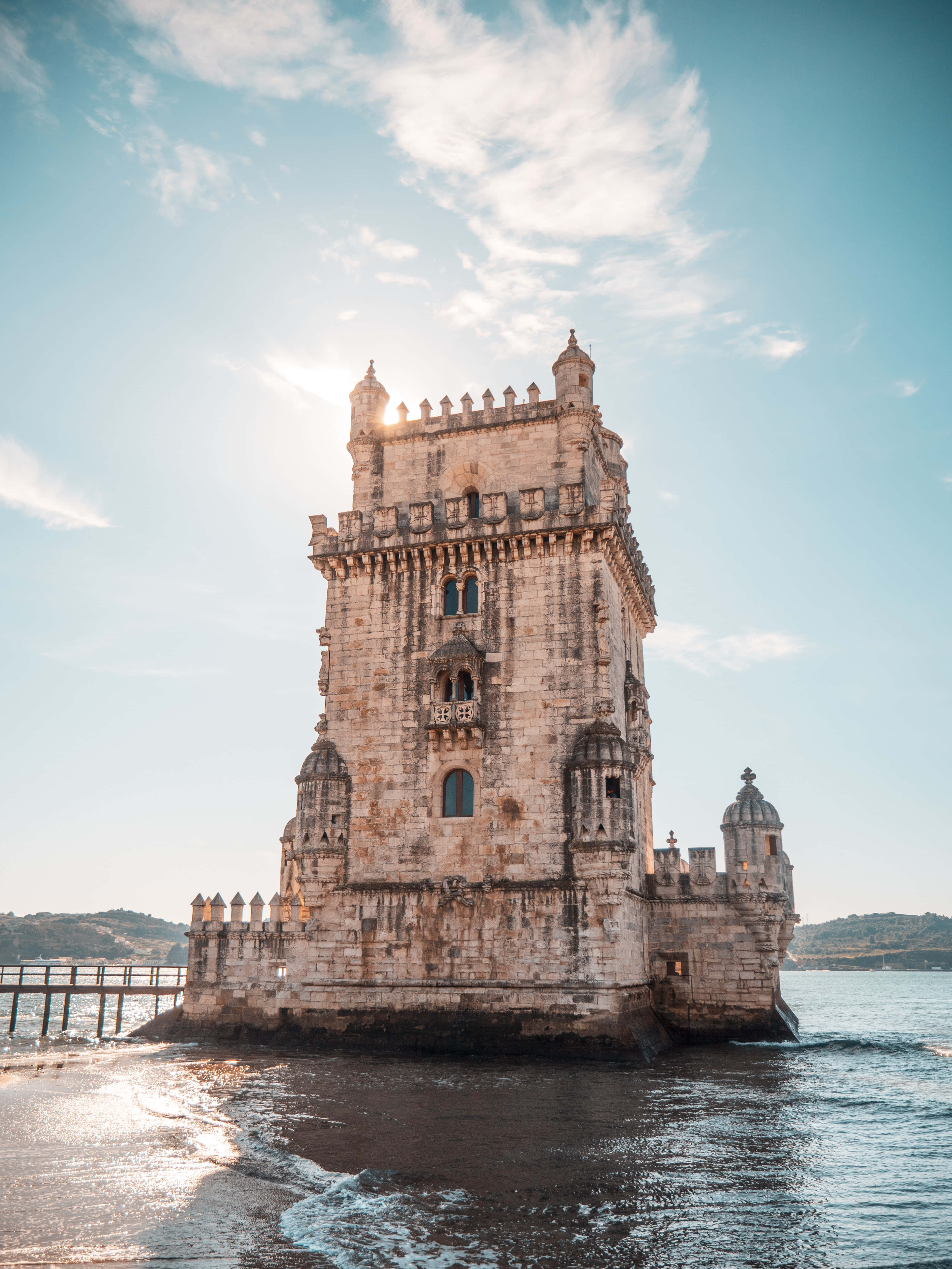 Portugal 桌布 壁紙 — 貝倫塔在薄雲和金色陽光的明亮藍天下，雄偉地矗立在塔霍河中。