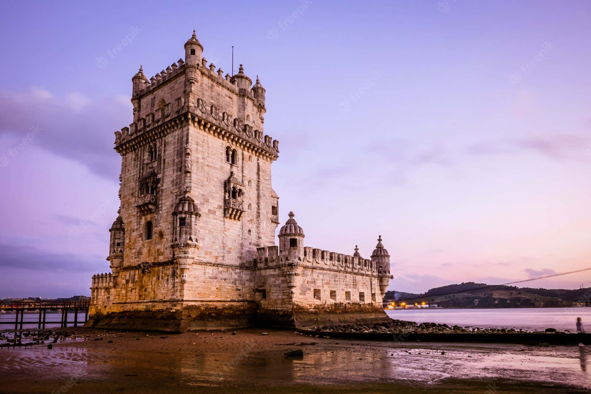 Portugal 桌布 壁紙 — 貝倫塔在黃昏時分巍然聳立，溫暖的燈光映照著紫色和粉紅色的天空，倒映在濕潤的泥灘上。
