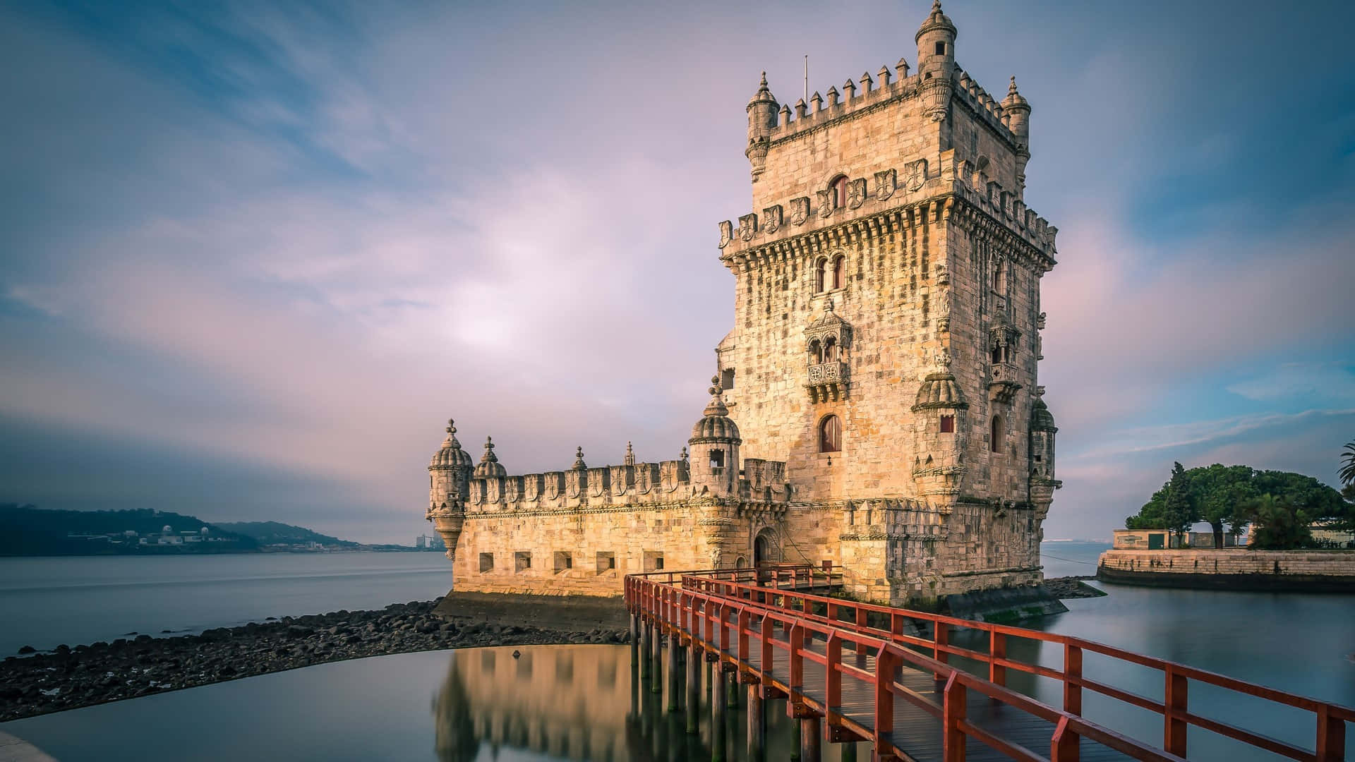 Portugal 桌布 壁紙 — 貝倫塔在黃昏時雄偉矗立，一座紅色橋樑通往其石質底座，在柔和暮色天空下平靜的水面上倒映。