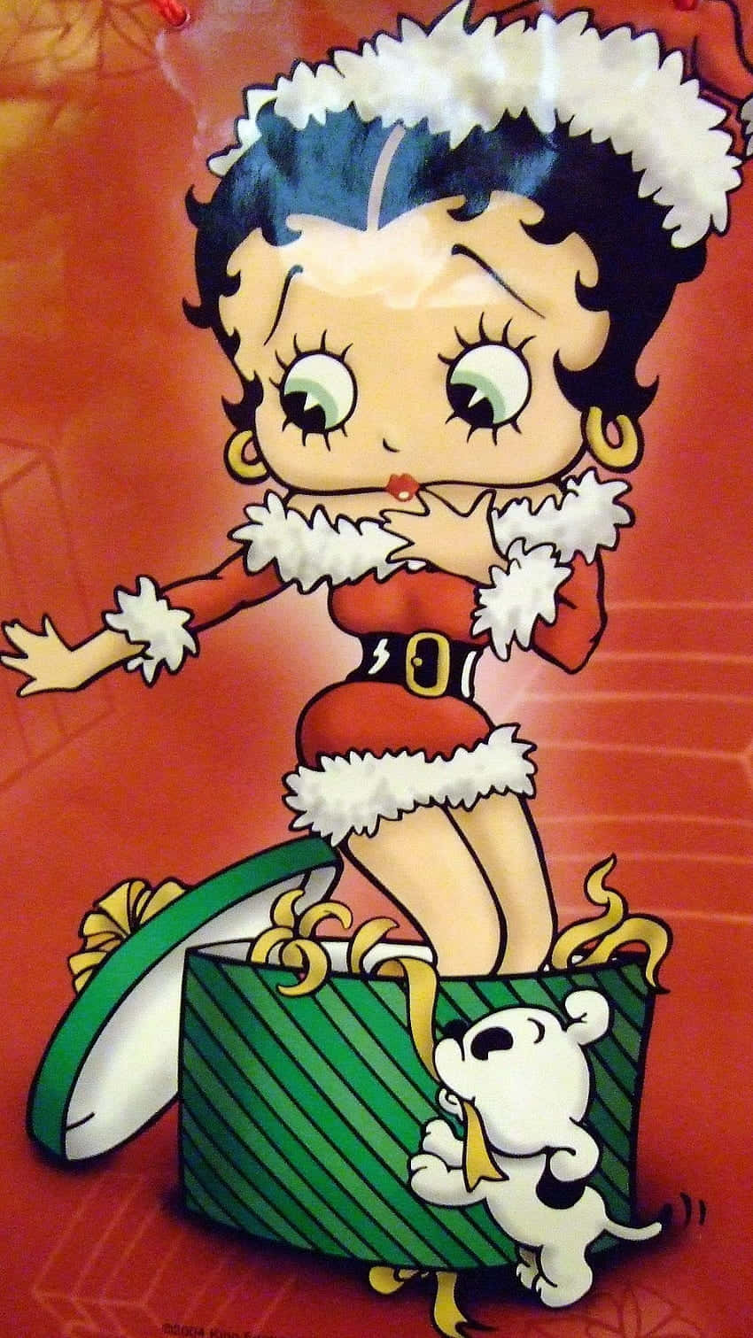 Betty Boop Christmas 桌布 壁紙 — 貝蒂娃娃穿著喜慶的紅色聖誕老人服裝，配有白色毛邊，從一個綠色條紋禮物盒中出現，旁邊有一隻頑皮的白色小狗。