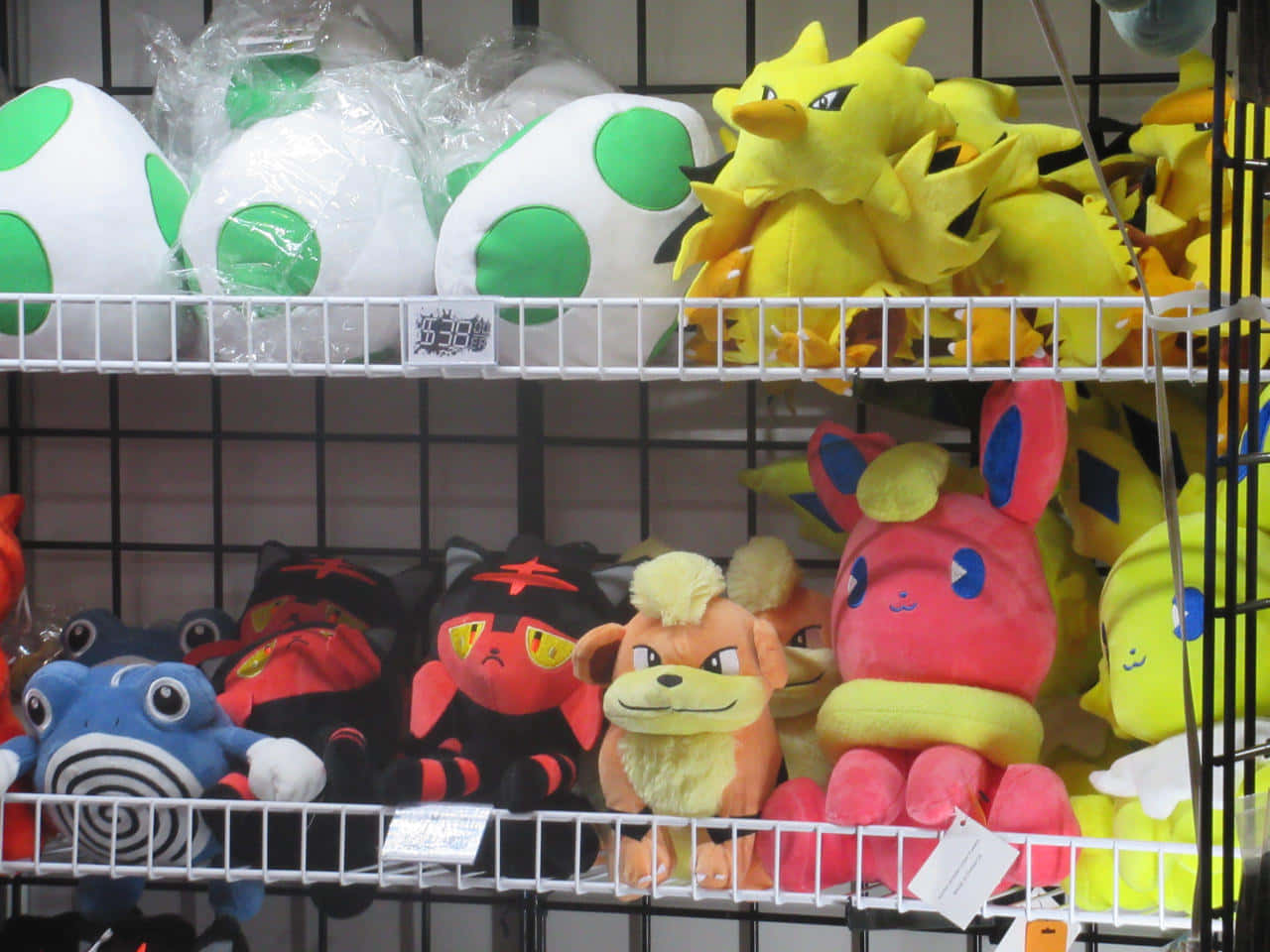 Pokemon Toys 桌布 壁紙 — 貨架上展示色彩繽紛的寶可夢毛絨玩具，包括皮卡丘和耀西，在零售店環境中。