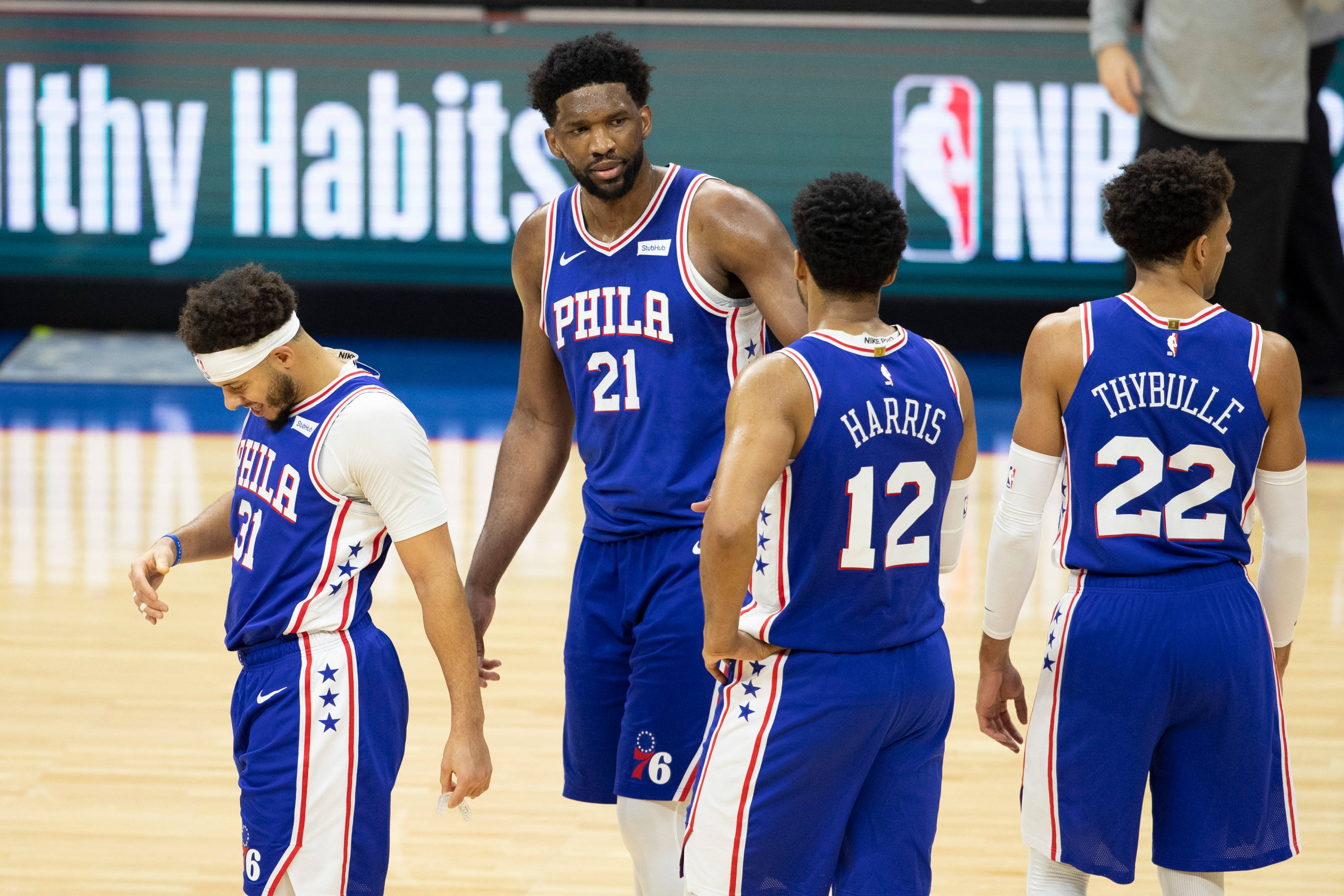 76ers 桌布 壁紙 — 費城76人籃球運動員身穿藍白球衣，在比賽期間聚集在拋光木地板上。
