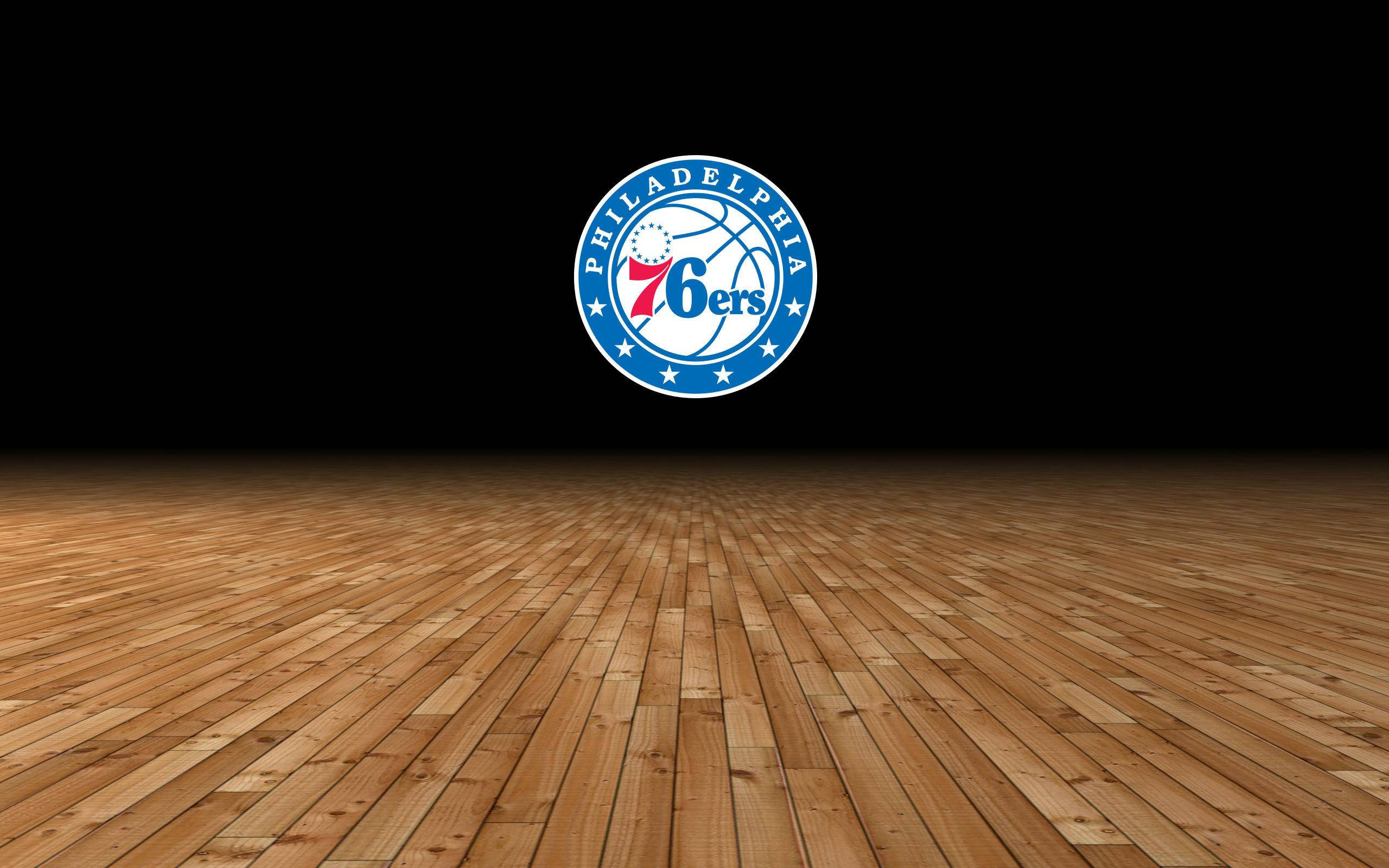 NBA 桌布 壁紙 — 費城76人隊標誌居中位於拋光木質籃球場地上方，背景為黑色。
