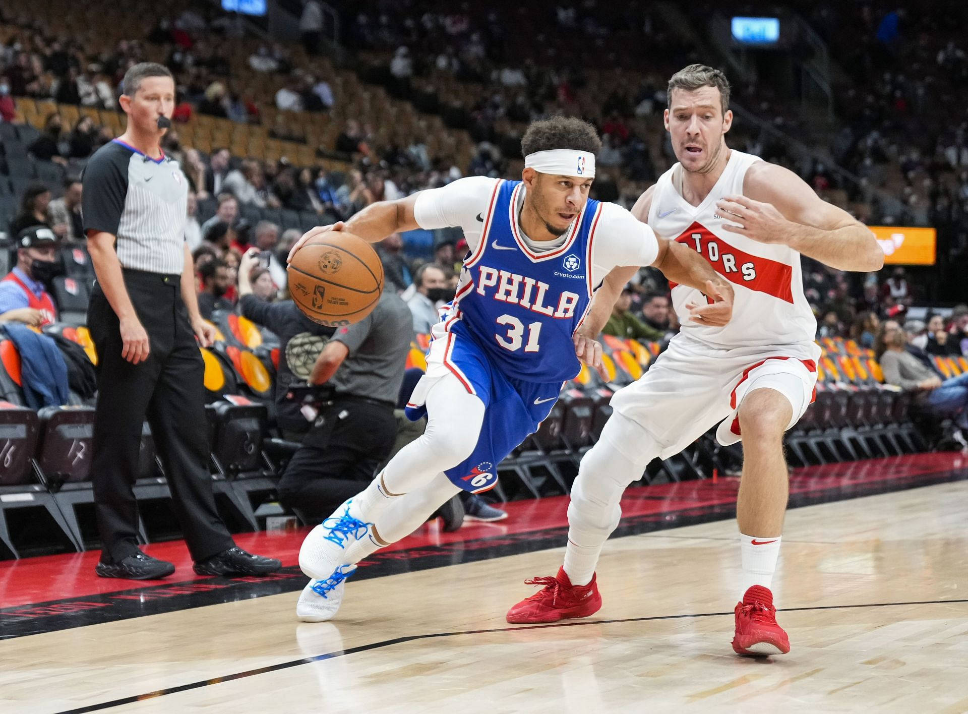 76ers 桌布 壁紙 — 費城76人隊球員身穿藍色球衣運球，同時被身穿白色的多倫多暴龍隊球員緊密防守，比賽激烈。