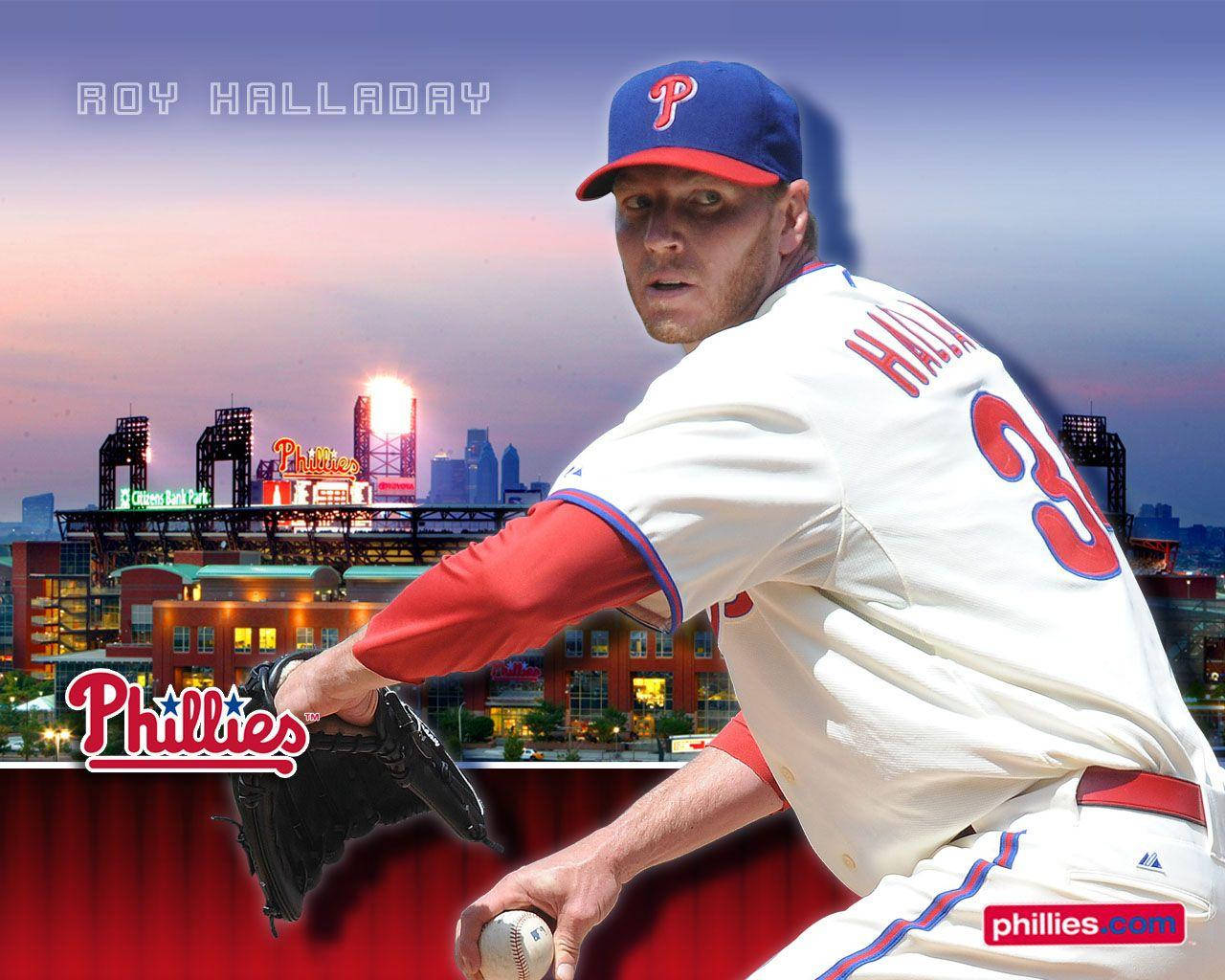 roy halladay 桌布 壁紙 — 費城人隊投手 Roy Halladay 身穿費城人隊球衣，在暮色城市天際線背景下投球，體育場燈光閃爍。