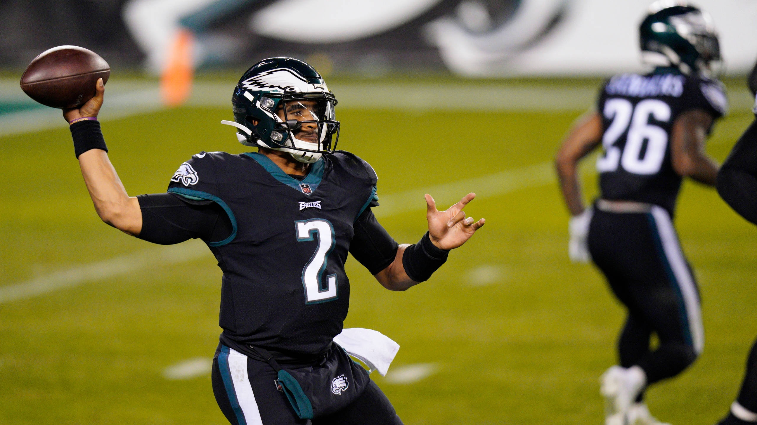 Jalen Hurts Eagles 桌布 壁紙 — 費城老鷹隊四分衛Jalen Hurts身穿黑色二號球衣，在綠色場地上的一場夜間比賽中投擲橄欖球。