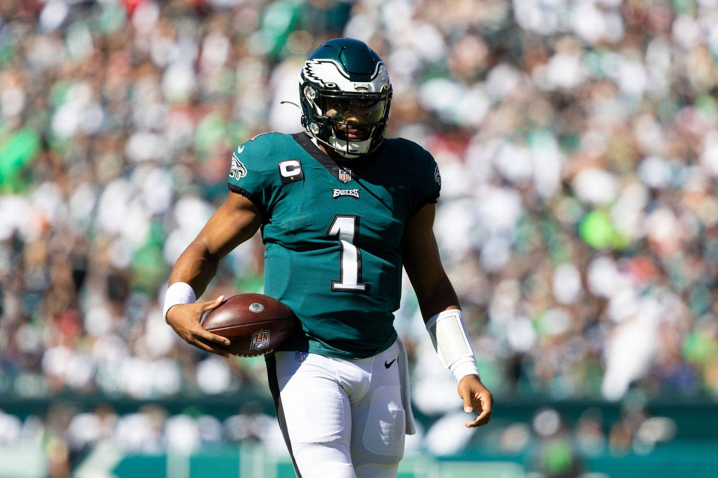 Jalen Hurts Eagles 桌布 壁紙 — 費城老鷹隊四分衛身穿青綠色一號球衣，在陽光明媚的球場上手持橄欖球。