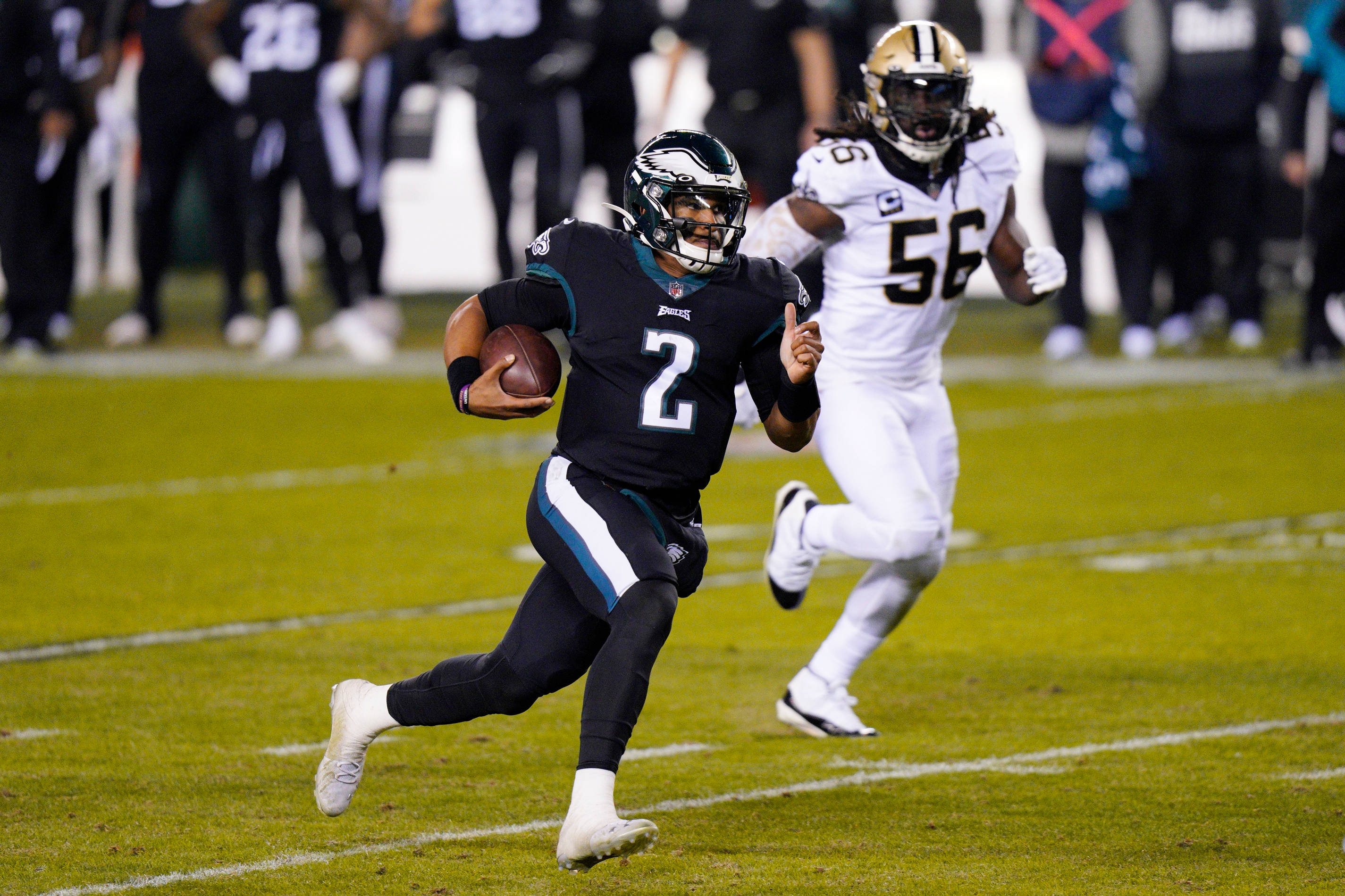 Jalen Hurts Eagles 桌布 壁紙 — 費城老鷹隊的四分衛身穿黑色球衣，在綠色球場上持球奔跑，同時被舊金山49人隊的防守球員追趕。