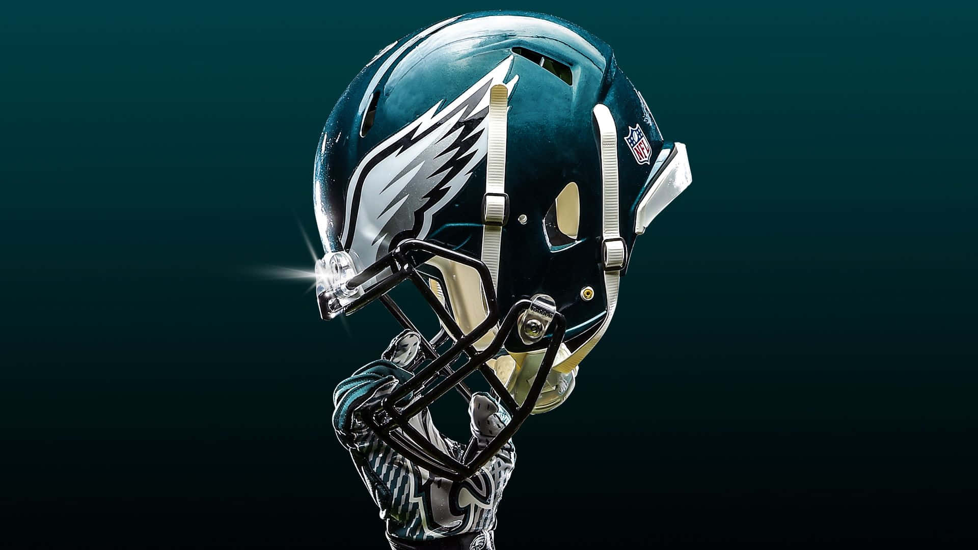Eagles Football 桌布 壁紙 — 費城老鷹隊美式足球頭盔在聚光燈下閃耀，背景為深藍綠色漸變。