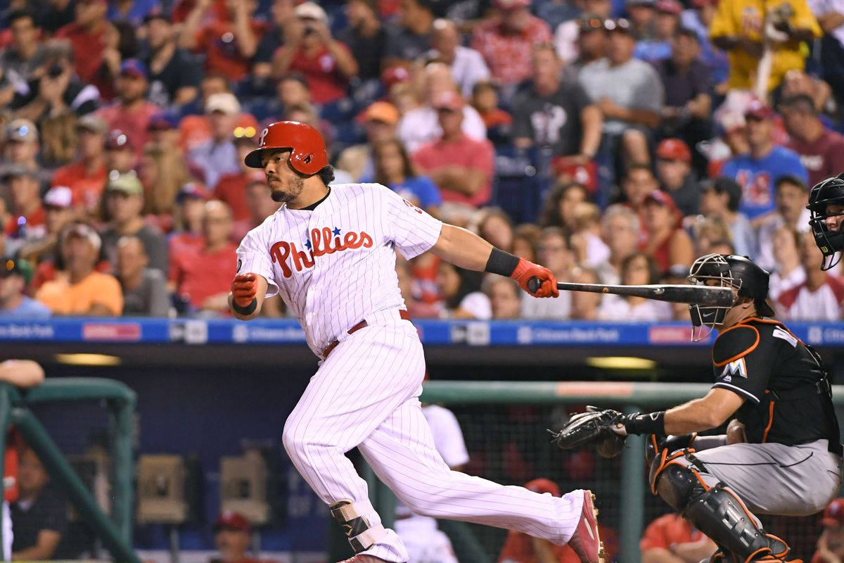 Phillies 桌布 壁紙 — 費城費城人隊的棒球選手在夜間比賽中強力揮棒，捕手和觀眾專注觀看。