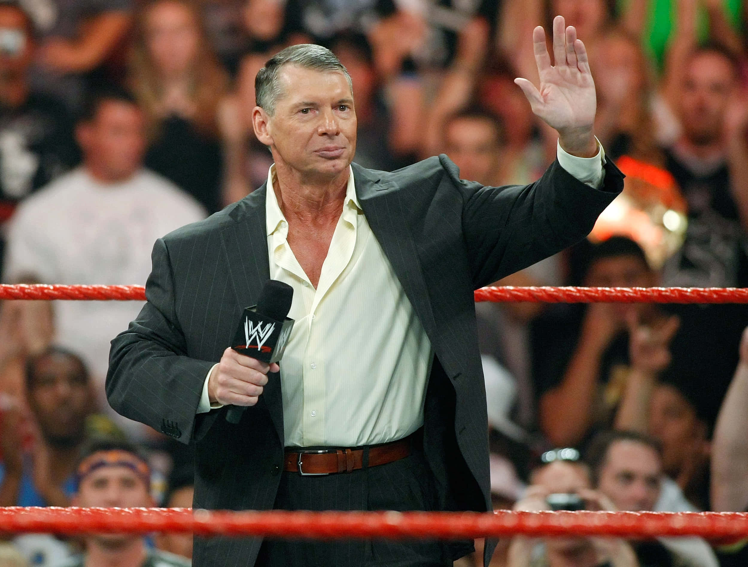 WWE 桌布 壁紙 — 資深摔角評論員 Vince McMahon 在燈光明亮、帶有紅色繩索的摔角場內向粉絲揮手。